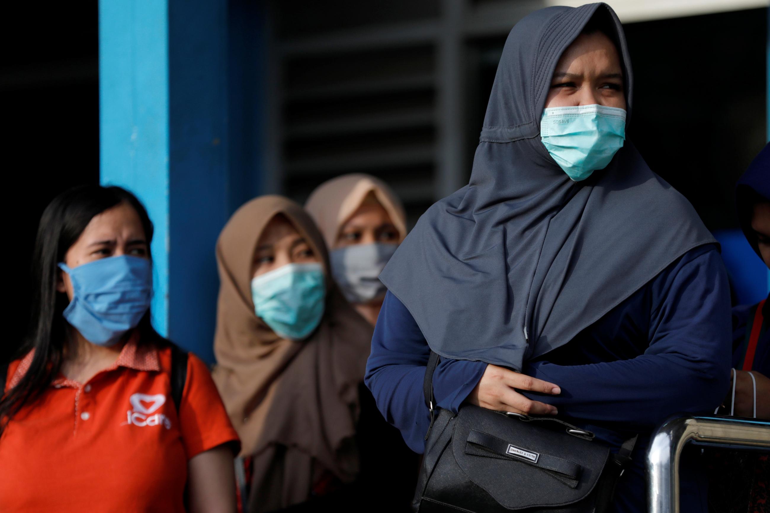 Women wearing face masks stand as they queue for public bus amid the spread of coronavirus disease in Jakarta, Indonesia March 18, 2020.