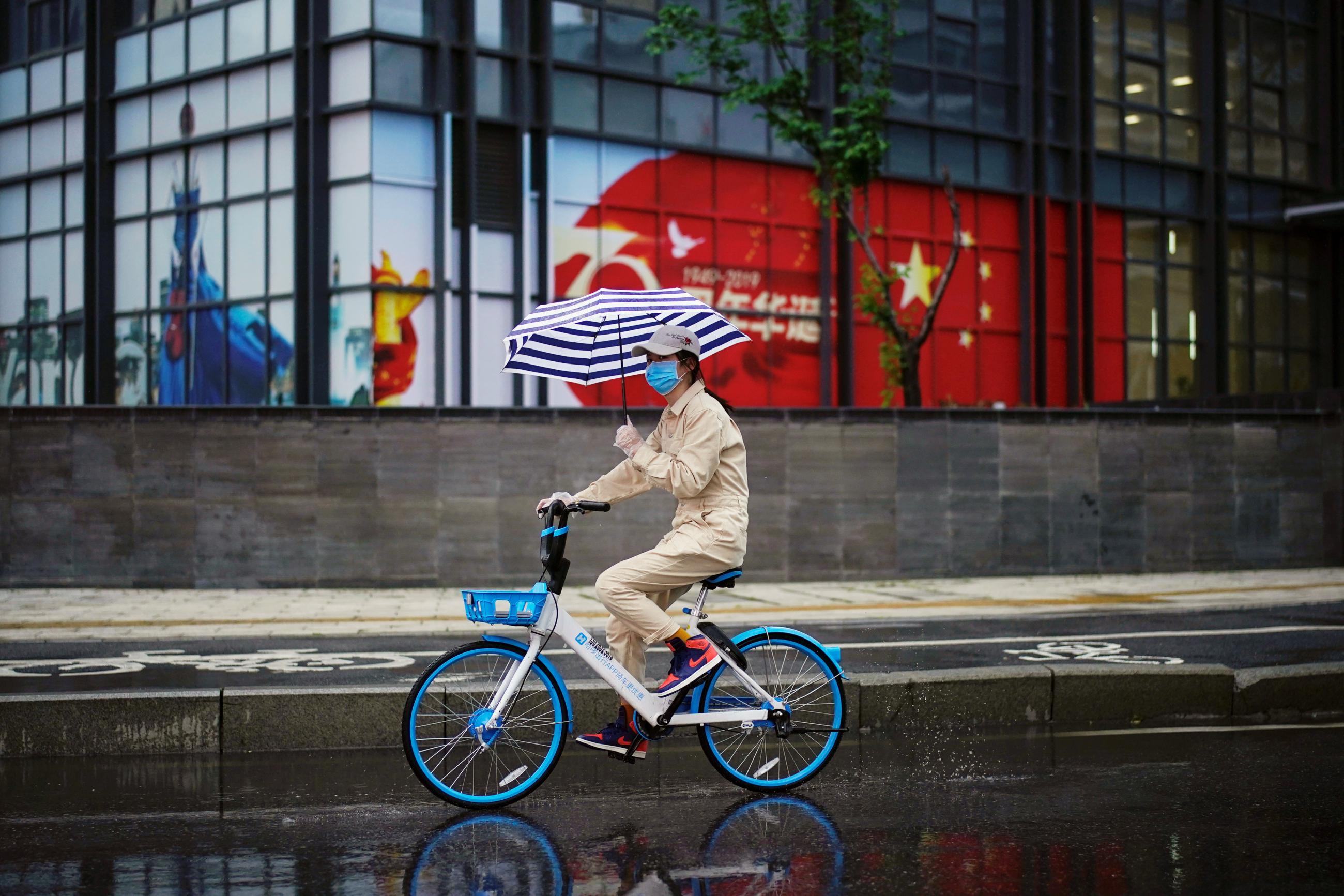 A woman holding an umbrella rides a shared bicycle past an image of the Chinese flag after the lockdown was lifted in Wuhan, the capital of Hubei province and China's epicentre of the novel coronavirus disease (COVID-19) outbreak, April 10, 2020.