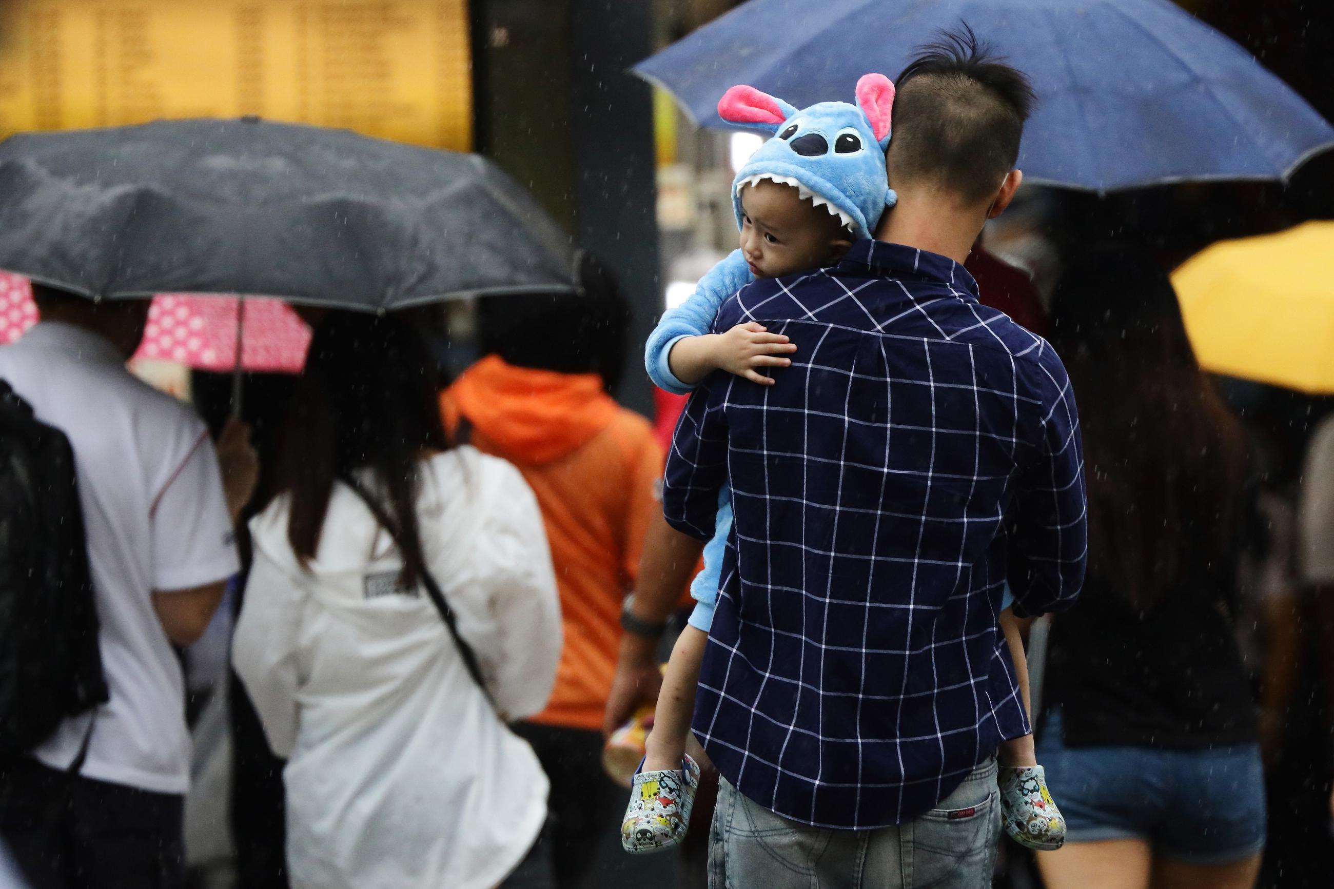 A parent carrying a child dressed in cartoon themed pajamas crosses a street in the rain in Singapore on January 10, 2021.