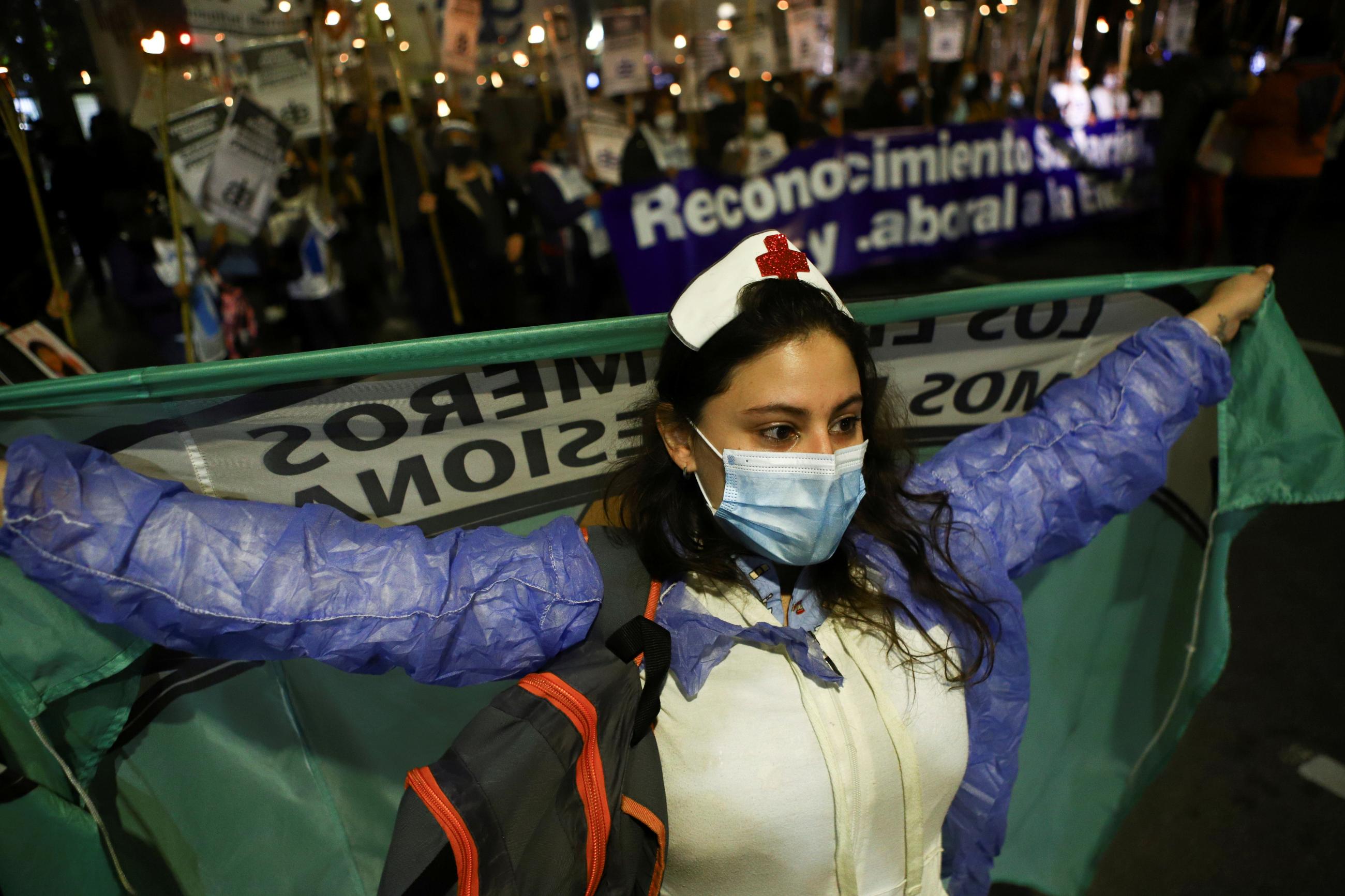 A nurse protests with other nurses in Buenos Aires, Argentina in May 2021. She is holding her arms out to the side carrying a protest banner.