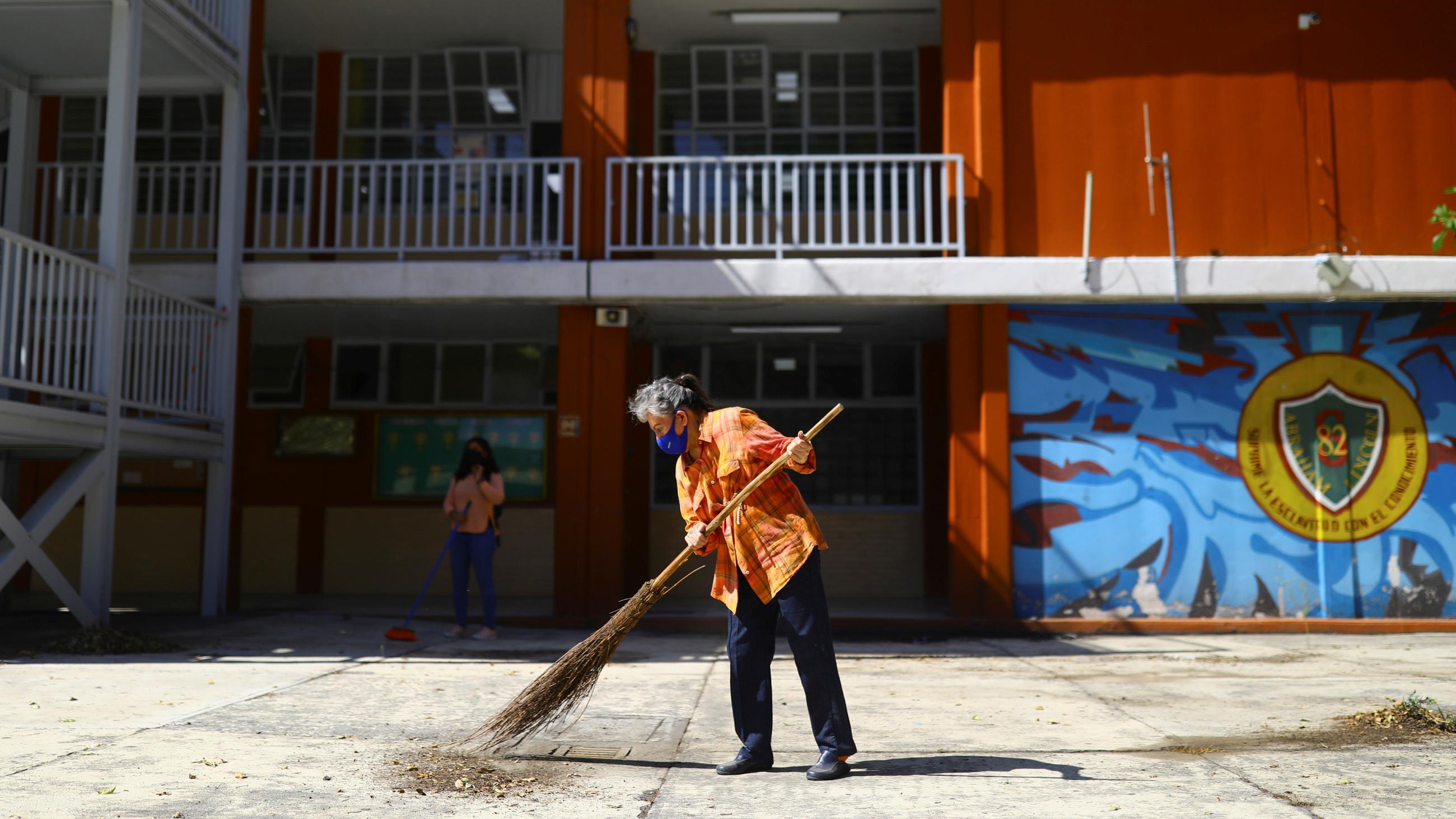 A parent sweeps a courtyard decorated in murals at Abraham Lincoln school before students return to class as part of Mexico City's reopening in May 2021.
