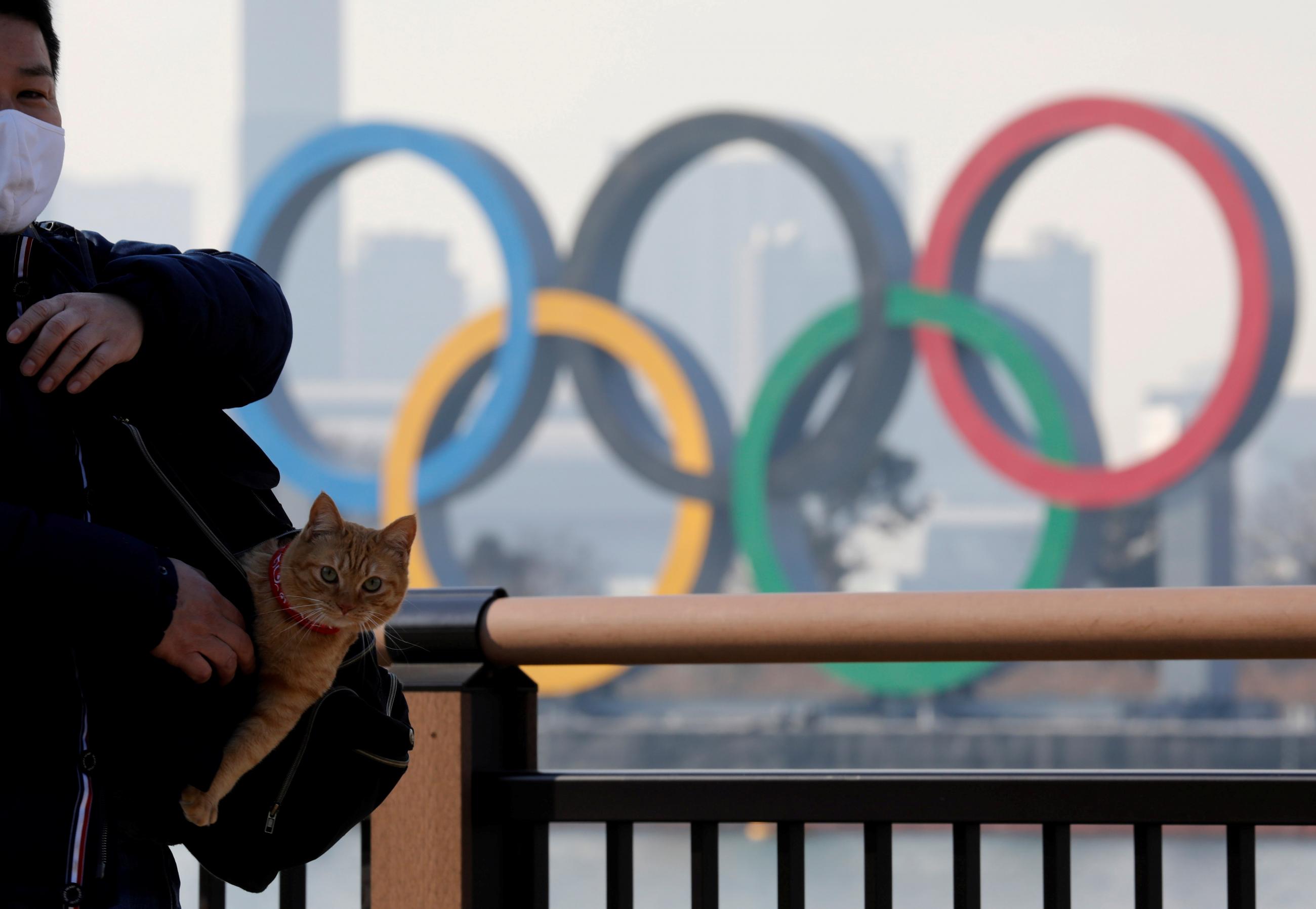 A man, accompanied by his cat, wears a mask to protect against COVID-19 while on a visit to a park with a view of the giant Olympic rings, in Tokyo, Japan on January 22, 2021.