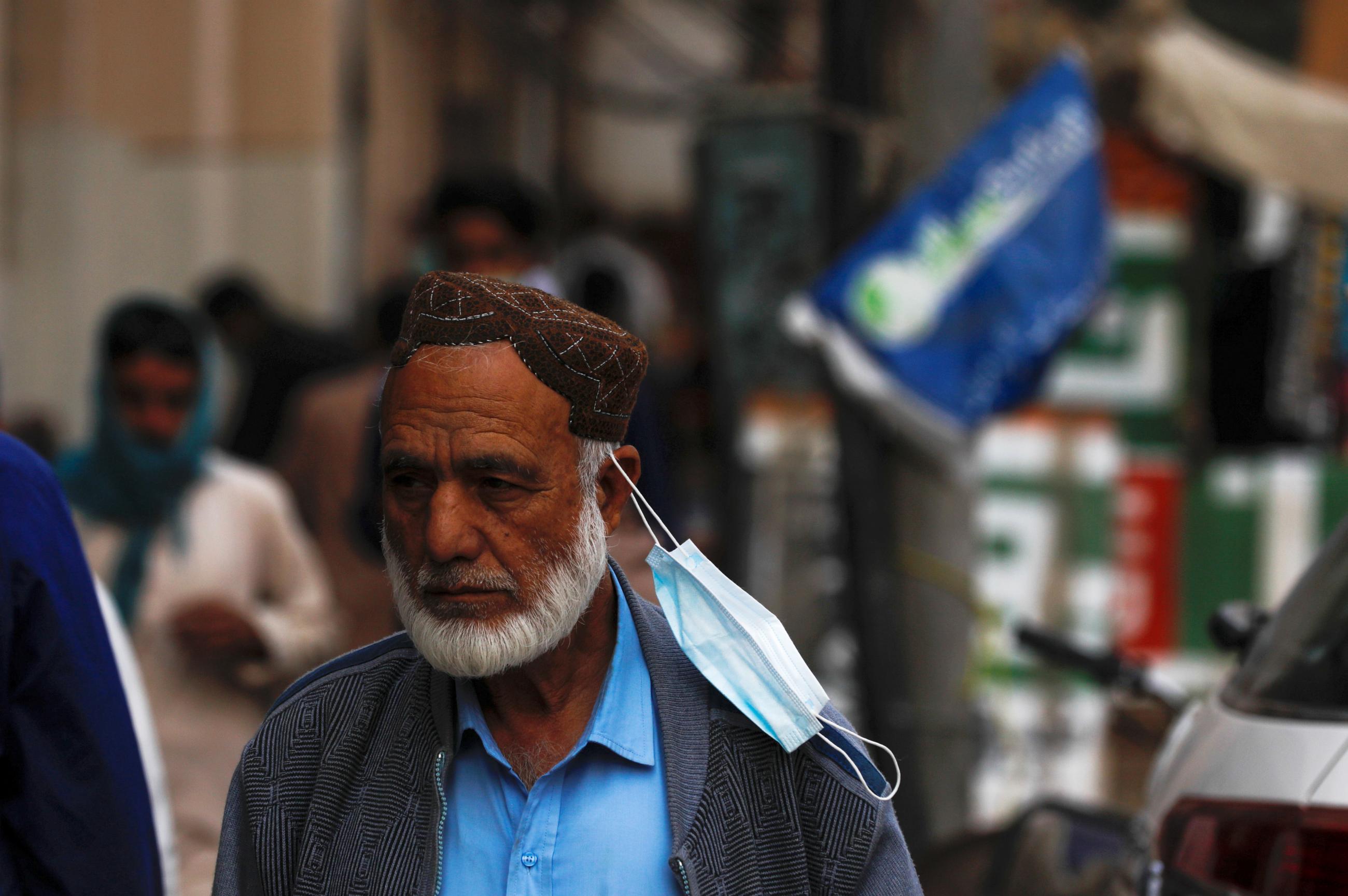 A man with a face mask hanging on his ear walks along a market as the outbreak of the coronavirus disease continues, in Karachi, Pakistan on January 15, 2021.