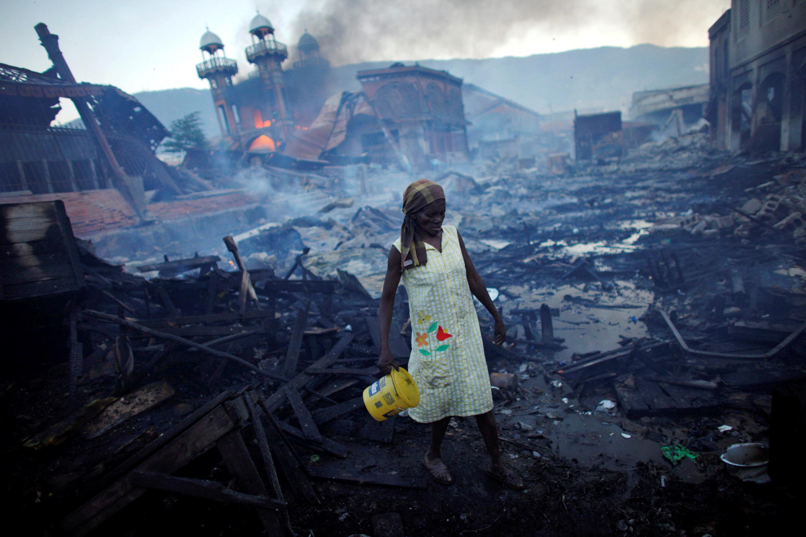A woman walks near a fire at the Hyppolite iron market in Port-au-Prince, Haiti, January 29, 2010. Picture taken January 29, 2010.