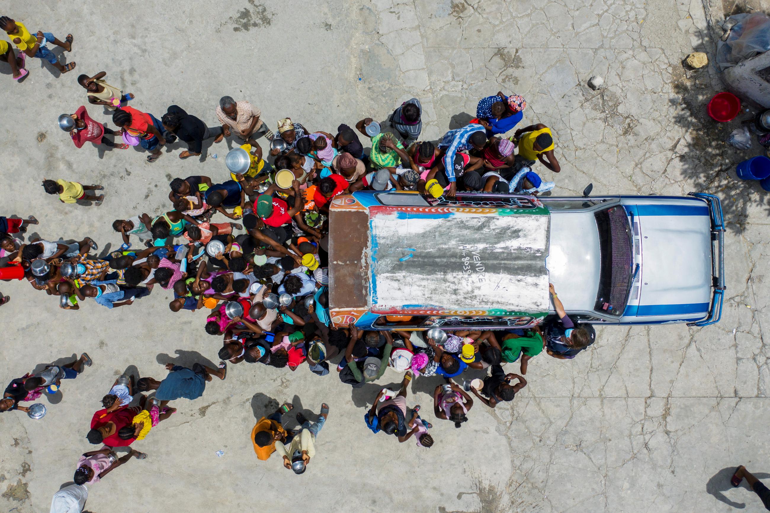 People gather around a car where volunteers distribute food to refugees at a shelter for families displaced by gang violence at the Saint Yves Church in Port-au-Prince, Haiti July 26, 2021