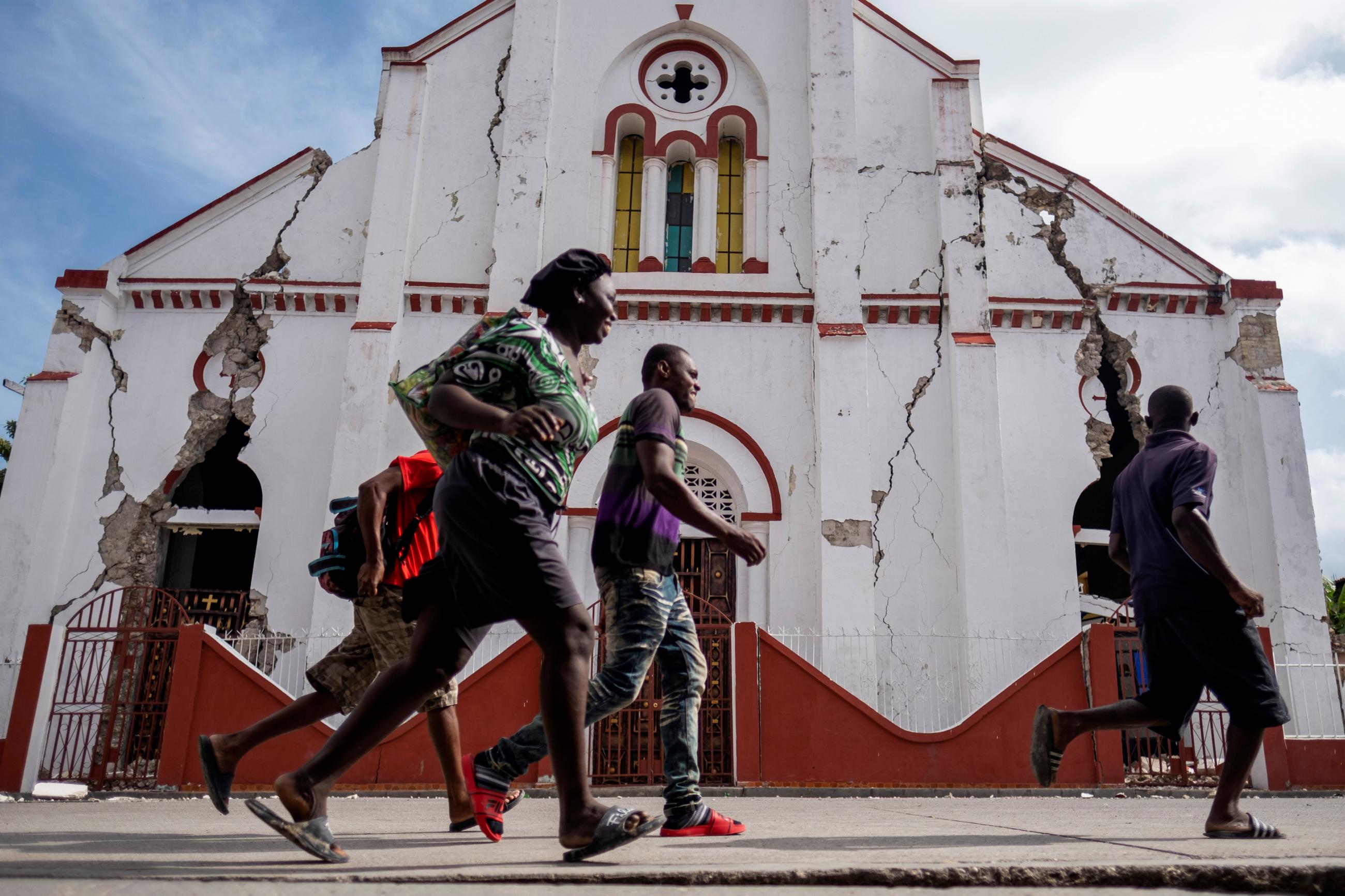 People run past a heavily damaged church after a 7.2 magnitude quake hit Les Cayes, Haiti, on August 18, 2021.