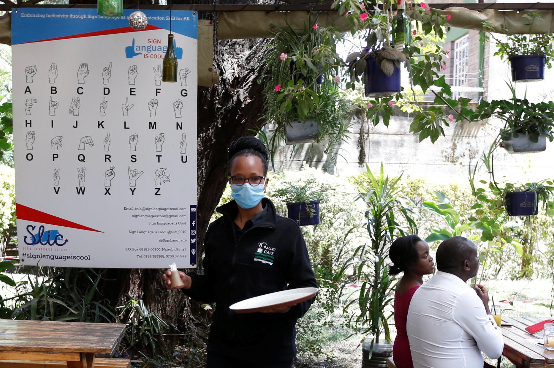 Deaf waitress Sharon Cherono walks past a sign language poster at the Pallet Cafe amid the COVID-19 pandemic, in the Lavington area of Nairobi, Kenya, on August 23, 2021. 