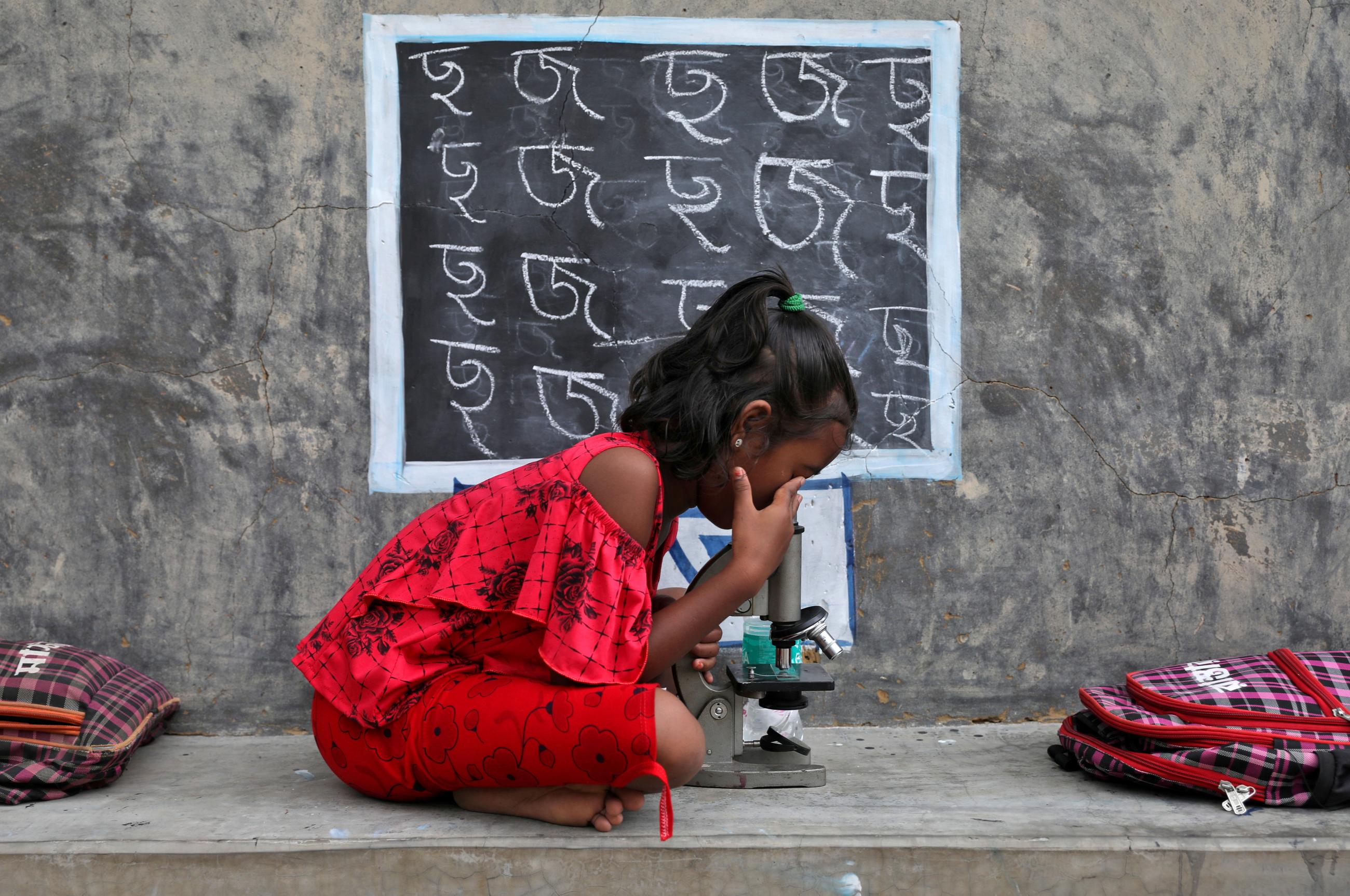 A young student uses a microscope as she attends a class outside of a home whose walls are converted into blackboards, in Joba Attpara village in West Bengal, India, on September 13, 2021.