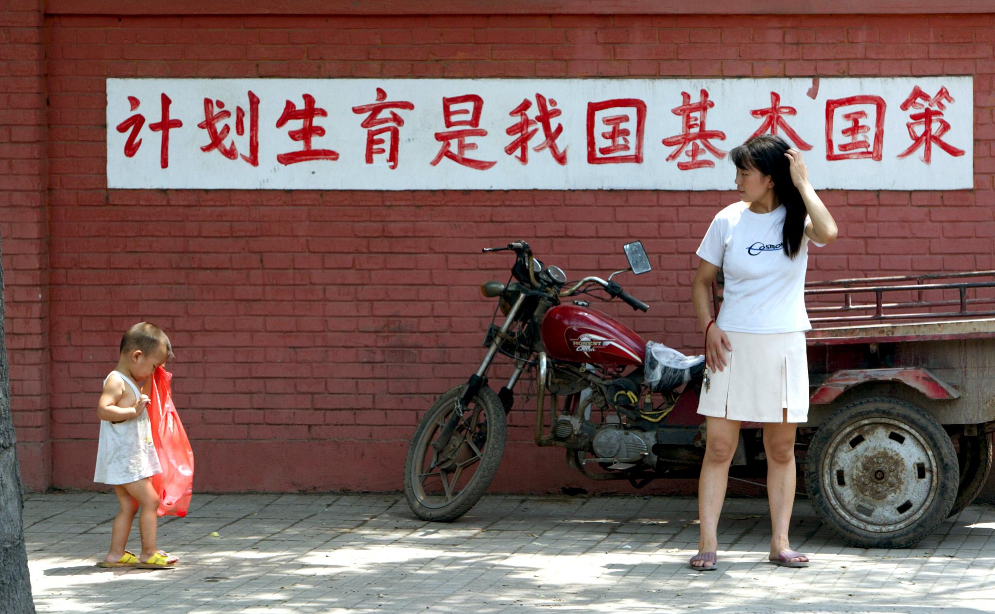A young Chinese mother watches her child in front of a sign reading "birth control is a basic state policy of our country" in Beijing July 23, 2002.