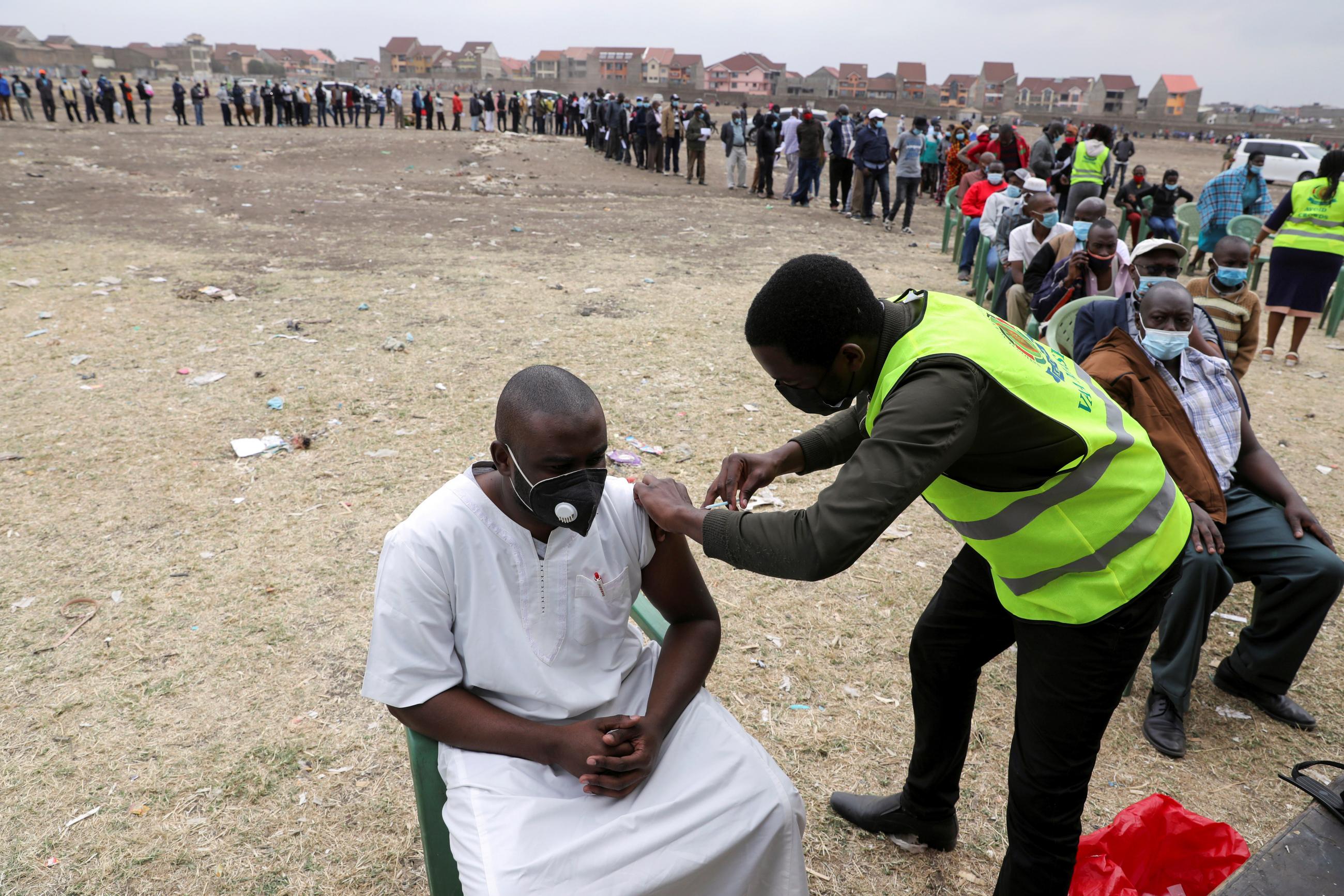 A health worker administers a UK-donated AstraZeneca/Oxford COVID-19 vaccine to a man in Nairobi, Kenya, as a long line of people wait behind them, on August 8, 2021. 