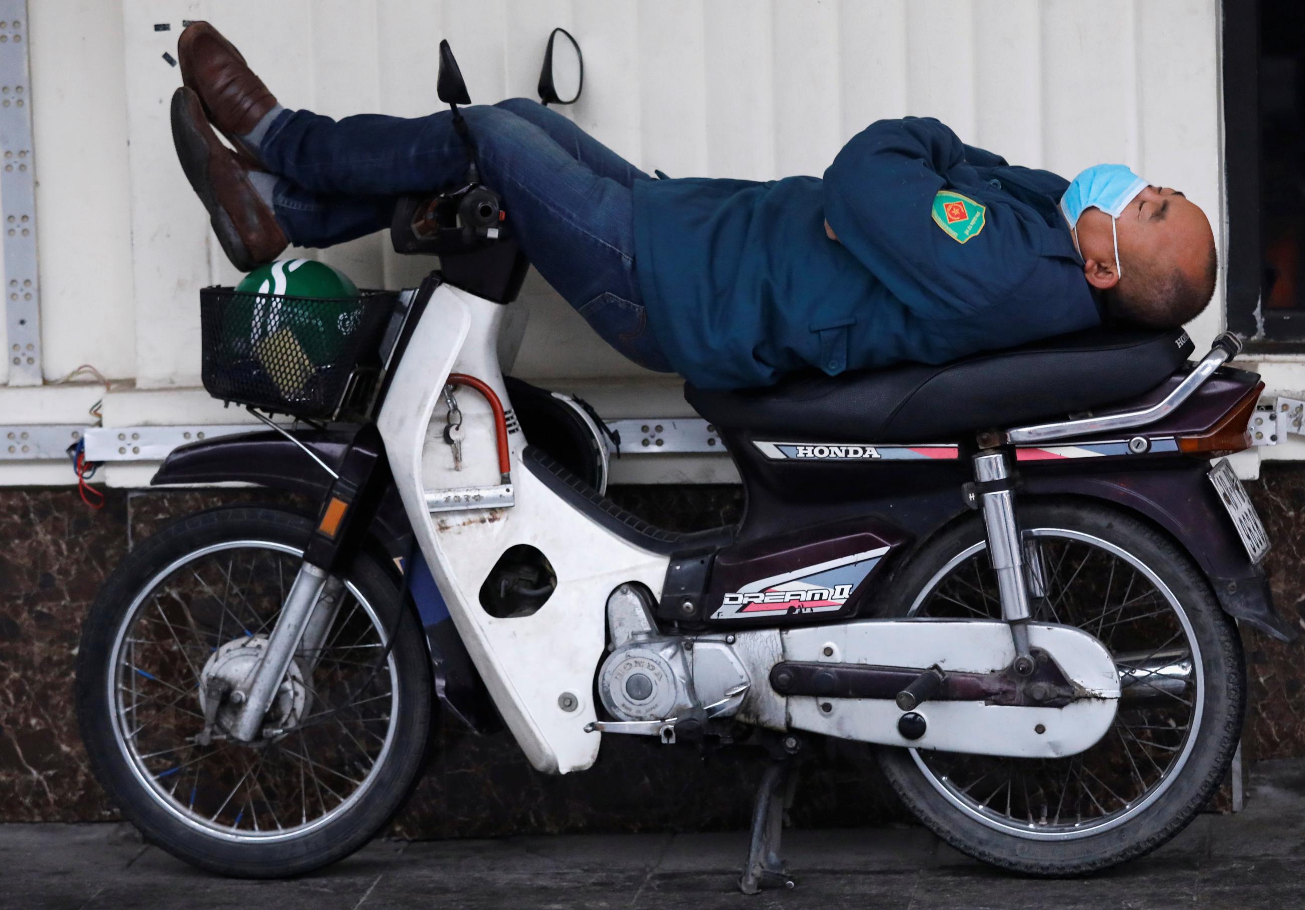 A man wears a protective mask in the early months of the COVID-19 pandemic while he takes a rest on his motorcycle on a street in Hanoi, Vietnam, on February 3, 2020.