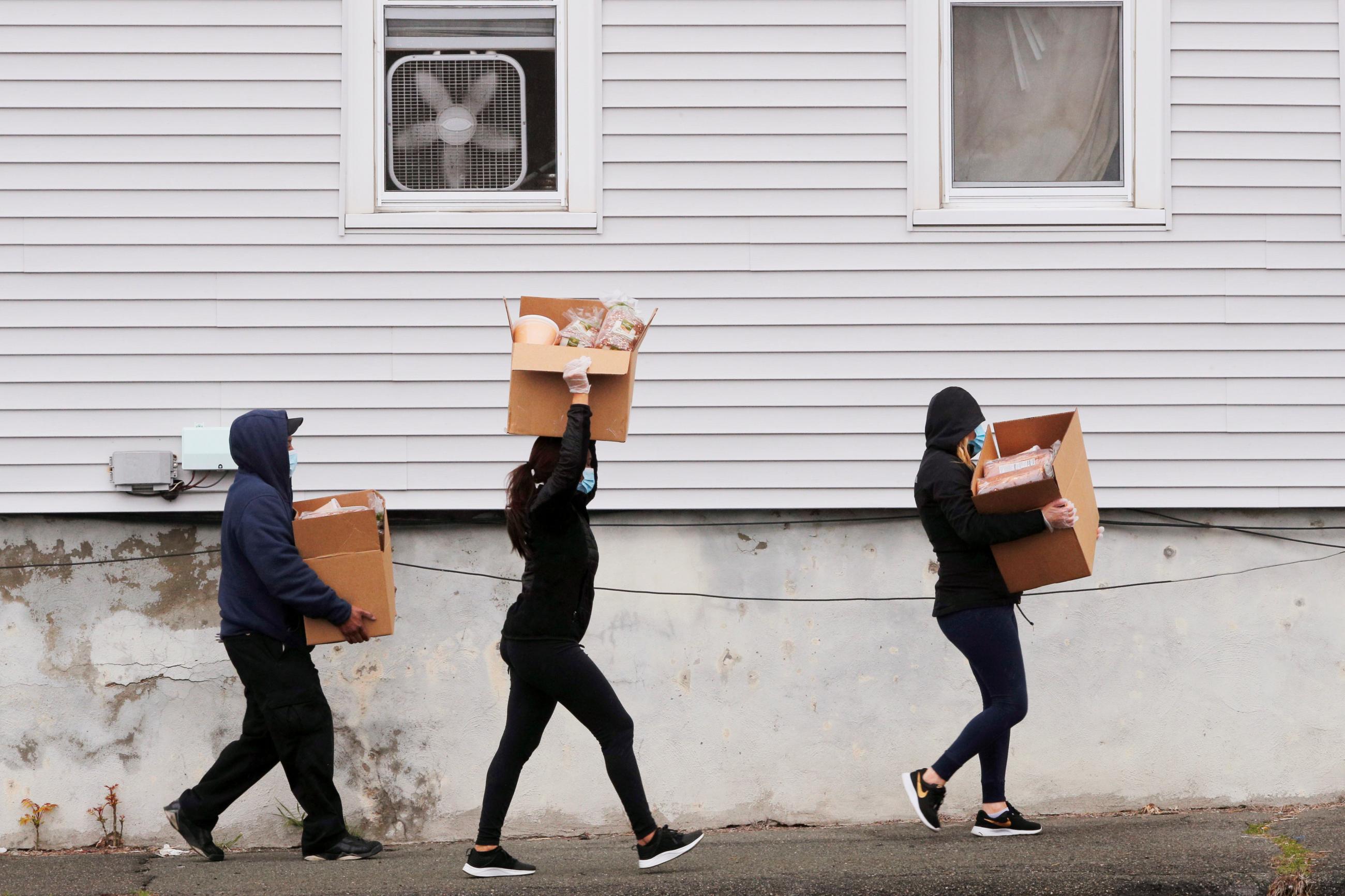 Three people carry large brown boxes of free groceries distributed at a pop-up food pantry by the 101st Engineer Battalion of the Massachusetts Army National Guard, in Chelsea, Massachusetts, on April 24, 2020.