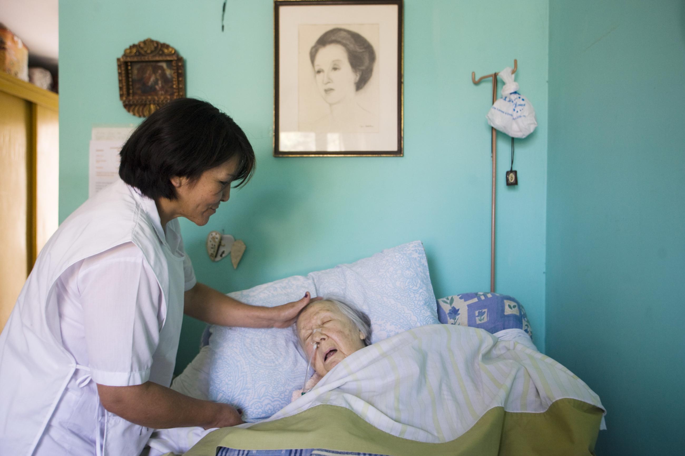 A nurse attends to an elderly woman in a home for older people with turquoise walls