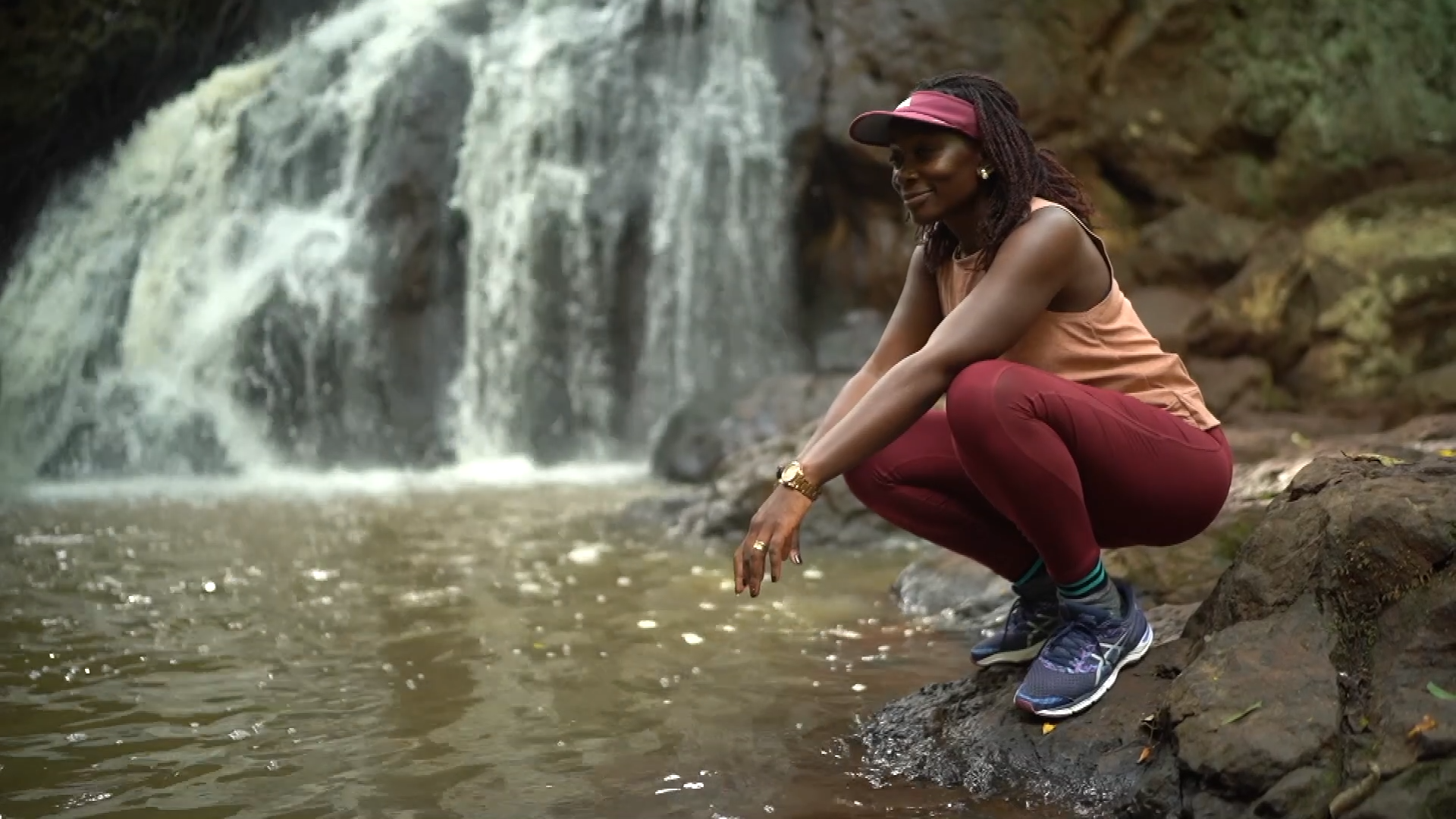 Dr. Liz Wangia sits next to a waterfall dressed in orange and red sportswear