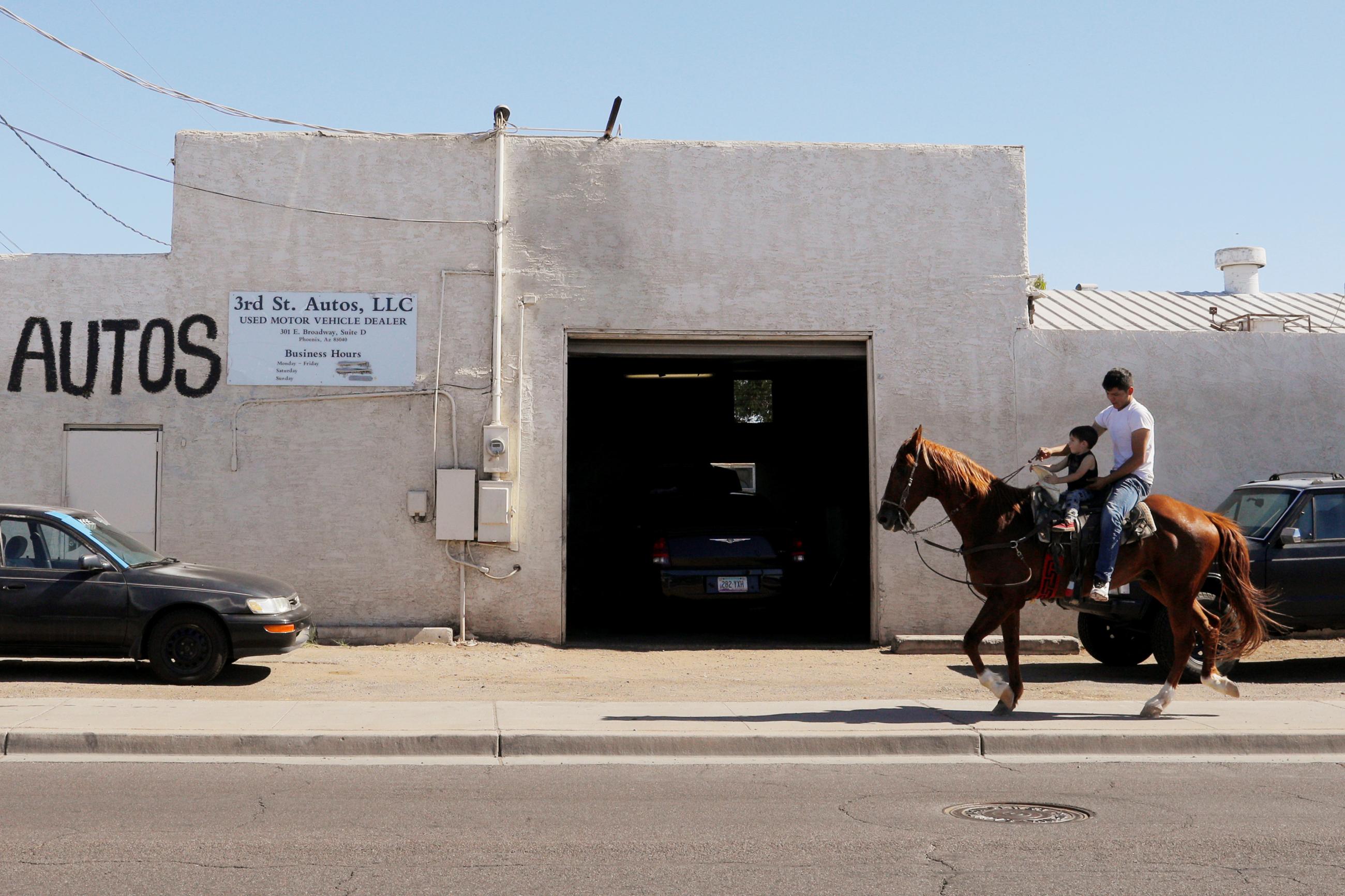 A man and his son ride a horse past an auto repair shop in the Maricopa County city of Phoenix, Arizona, on May 25, 2019.