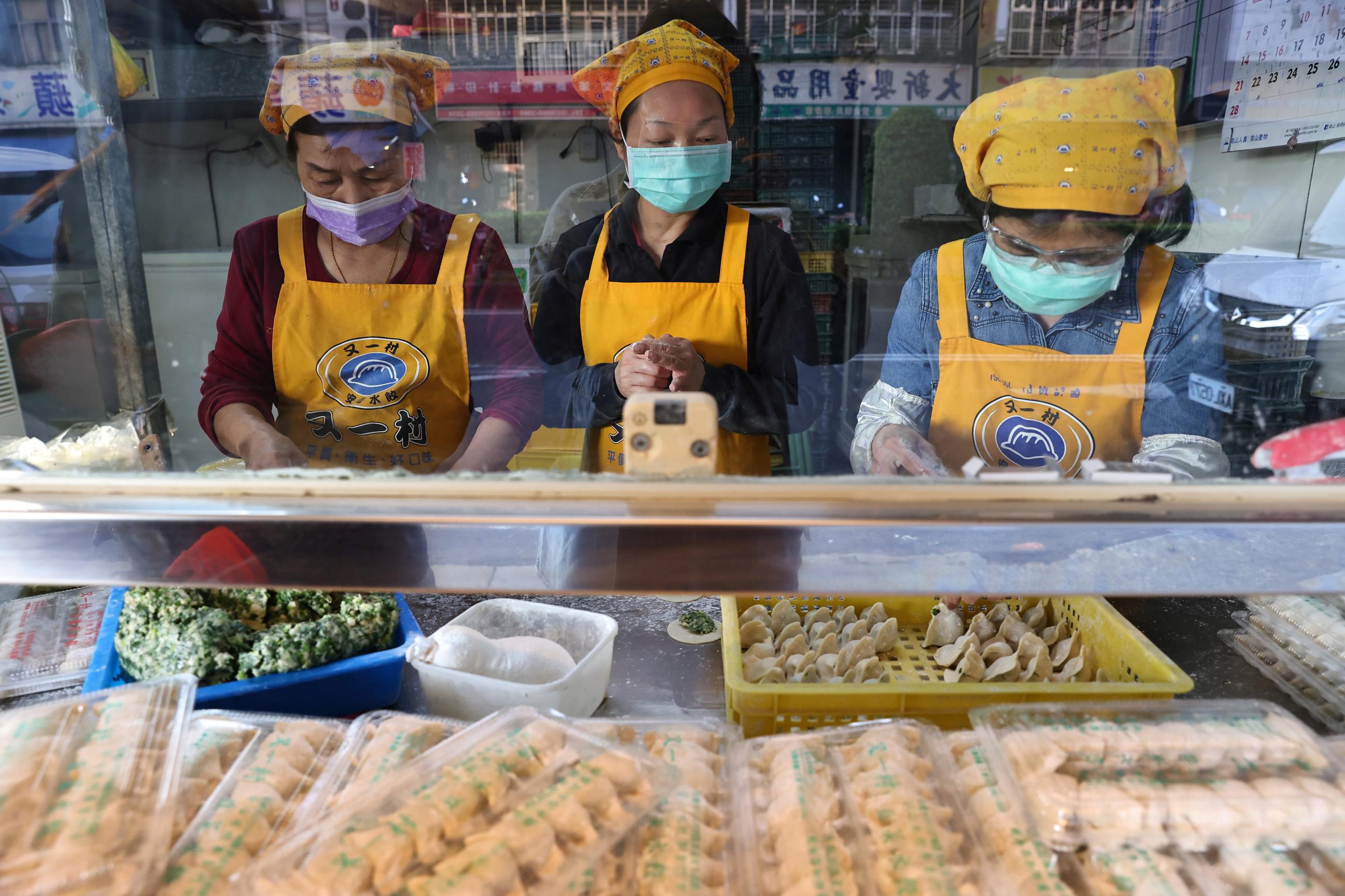 Three women in yellow aprons and COVID-19 masks make dumplings in a shop in Taiwan