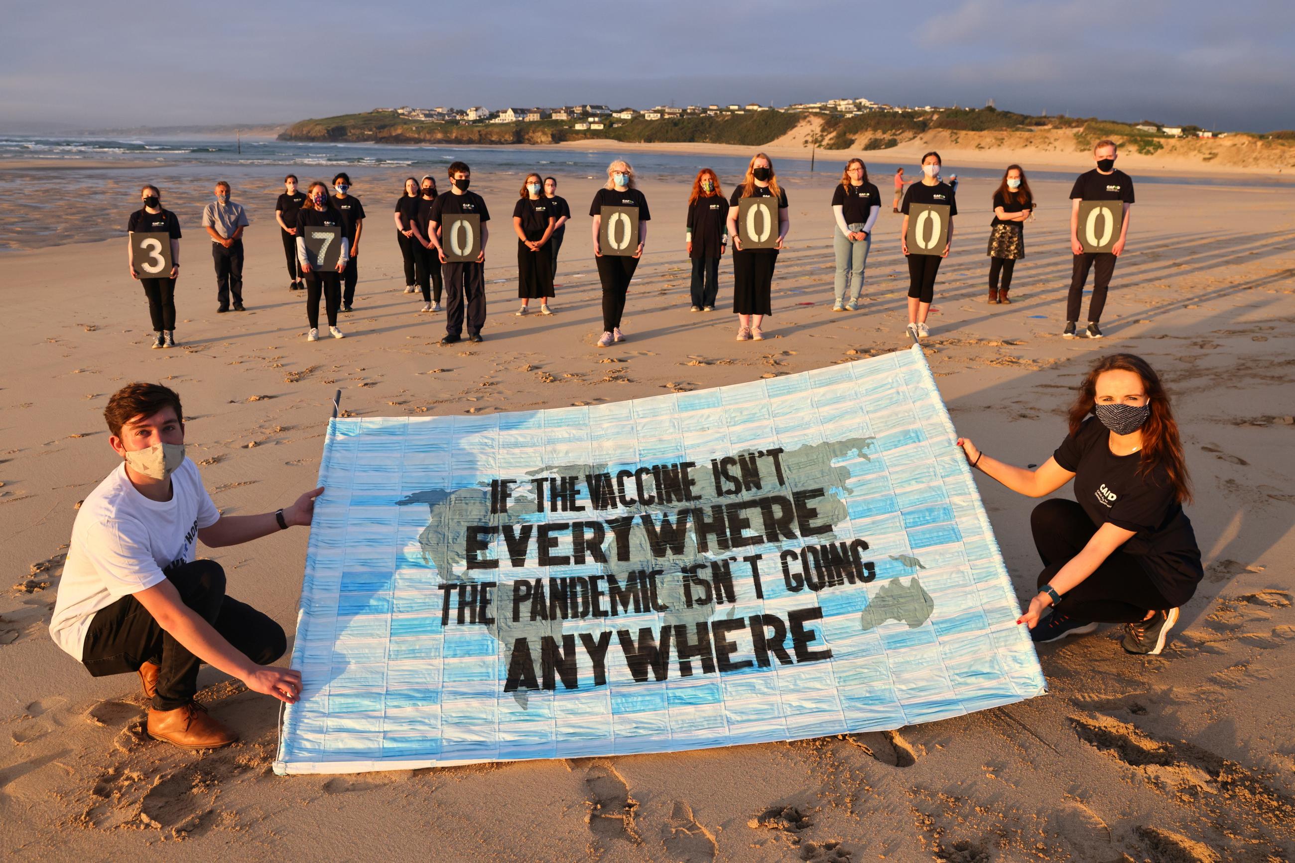 Activists hold a sign that reads, "If the vaccine isn't everywhere, the pandemic isn't going anywhere" on a beach in Cornwall, Britain.