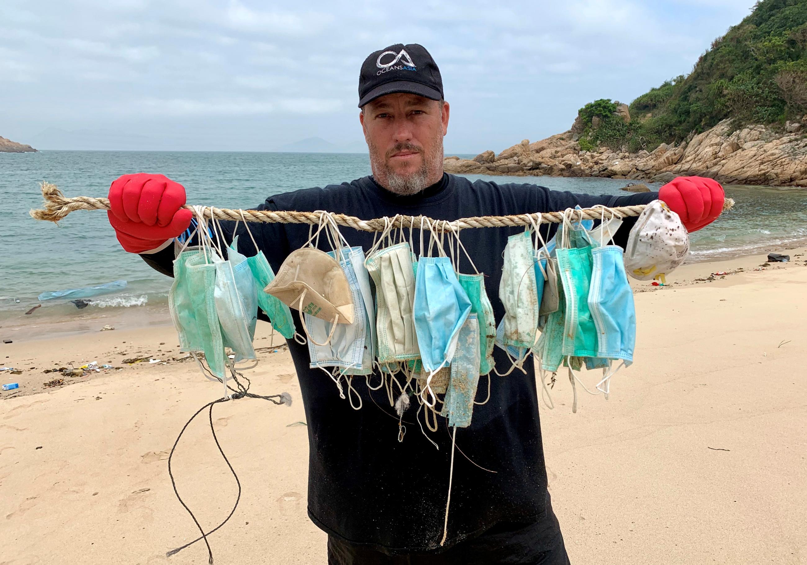 Gary Stokes, co-founder of marine conservation group OceansAsia, stands on a beach in the Soko Islands, holding green and blue medical masks that washed up following an outbreak of the novel coronavirus, in Hong Kong, China March 7, 2020.