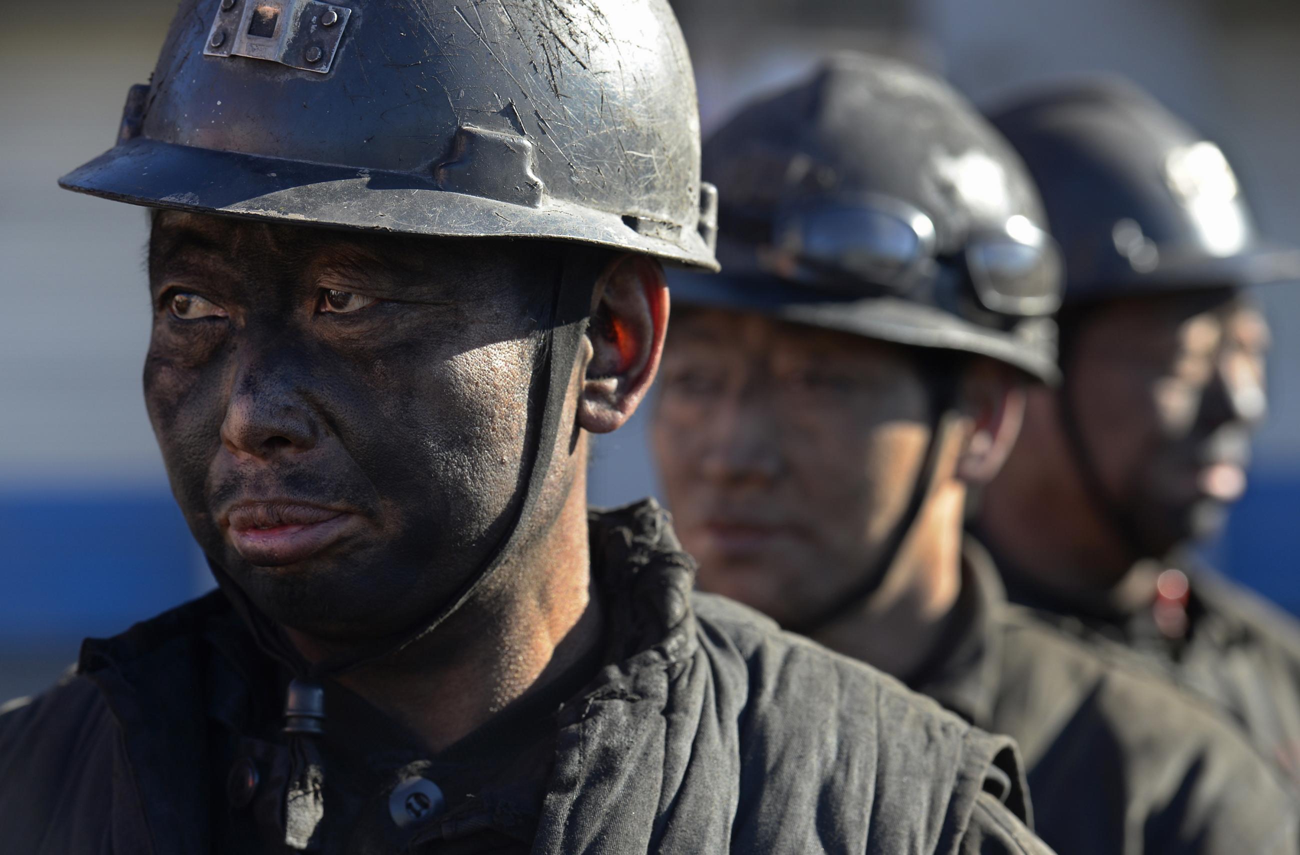 A close-up photo of the soot-covered faces of three coal miners wearing dark hard hats as they wait in line to shower during a break near a coal mine in Heshun county, Shanxi province, China, on December 5, 2014. 