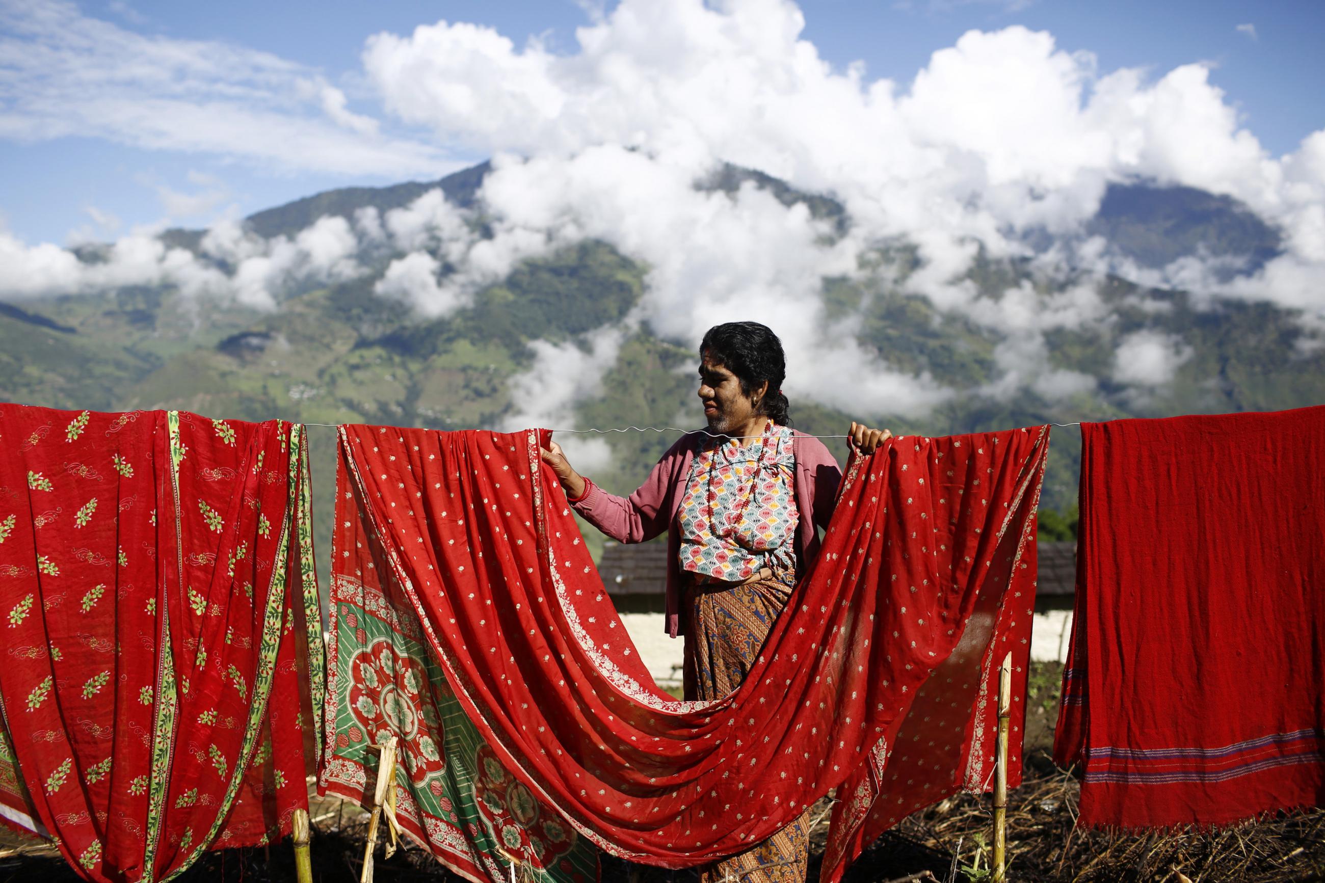 Devi Budhathoki, 38, hangs beautiful red fabric on a clothesline outside her house against a background of green mountains and fluffy white clouds and in Kharay, Dolkha District, 190 km (118 miles) northeast of Kathmandu September 15, 2013.