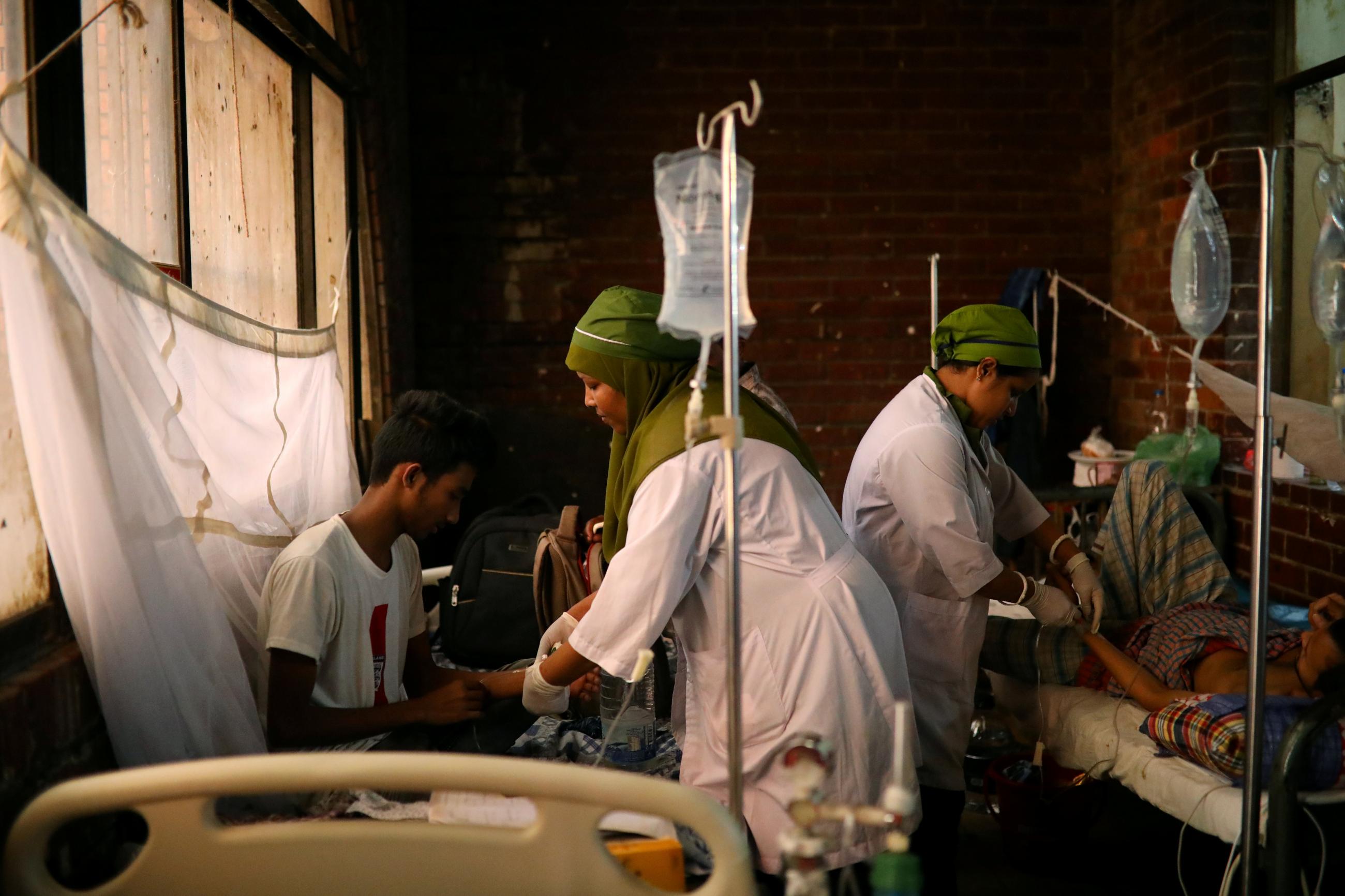 Nurses in white coats and green headscarves treat patients covered with mosquito nets who have been infected with dengue at the Shaheed Suhrawardy Medical College and Hospital in Dhaka, Bangladesh, August 2, 2019. 