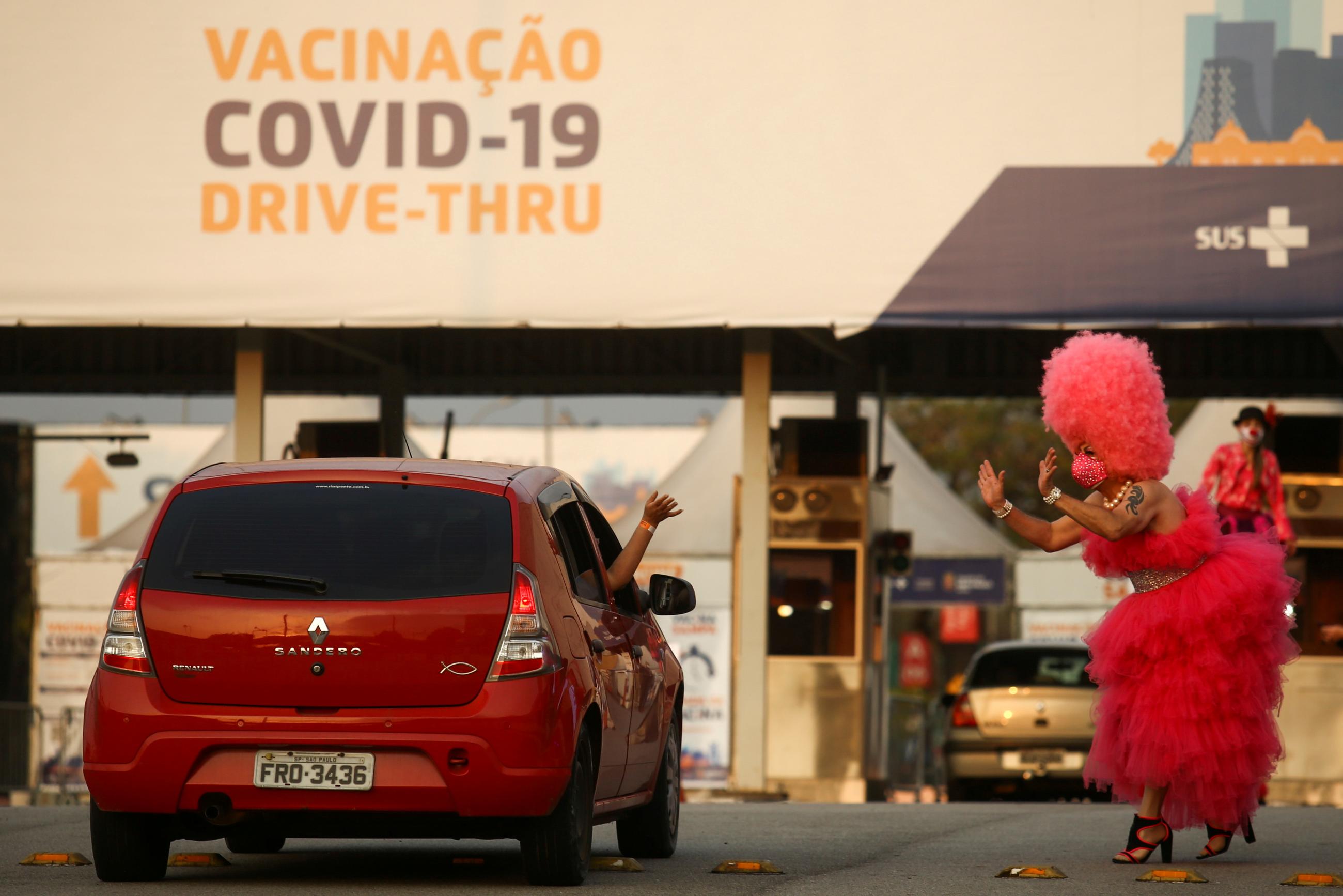 A drag queen in a tall pink wig and long pink dress waves to a car at a vaccine drive-thru as Sao Paulo begins to vaccinate young people from 18 to 21 years old against COVID-19, in Sao Paulo, Brazil on August 14, 2021. 