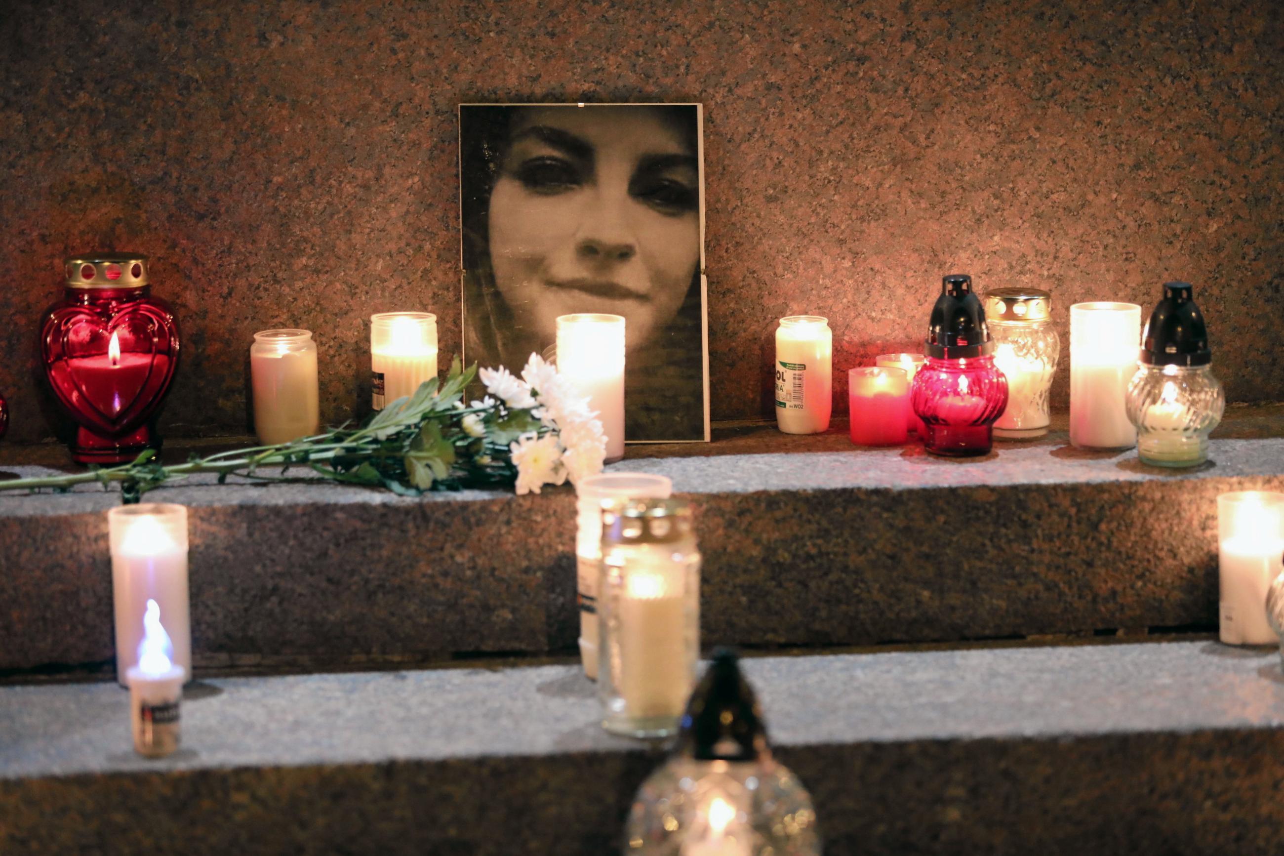A photo of Izabela, who died due to untreated complications from her pregnancy is leaned against a wall, surrounded by red and white candles in glass holders and white carnations