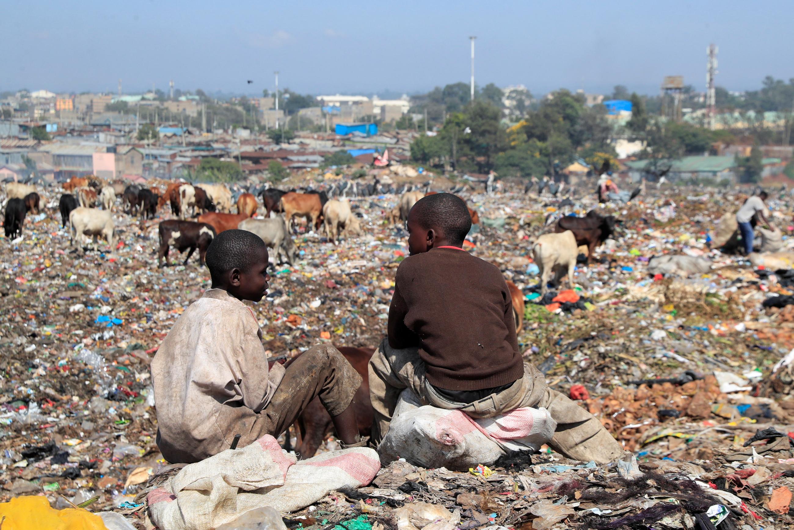 Two young boys sit on top of mountains of plastic waste with their backs turned to the camera in Nairobi, Kenya, in February 2022.