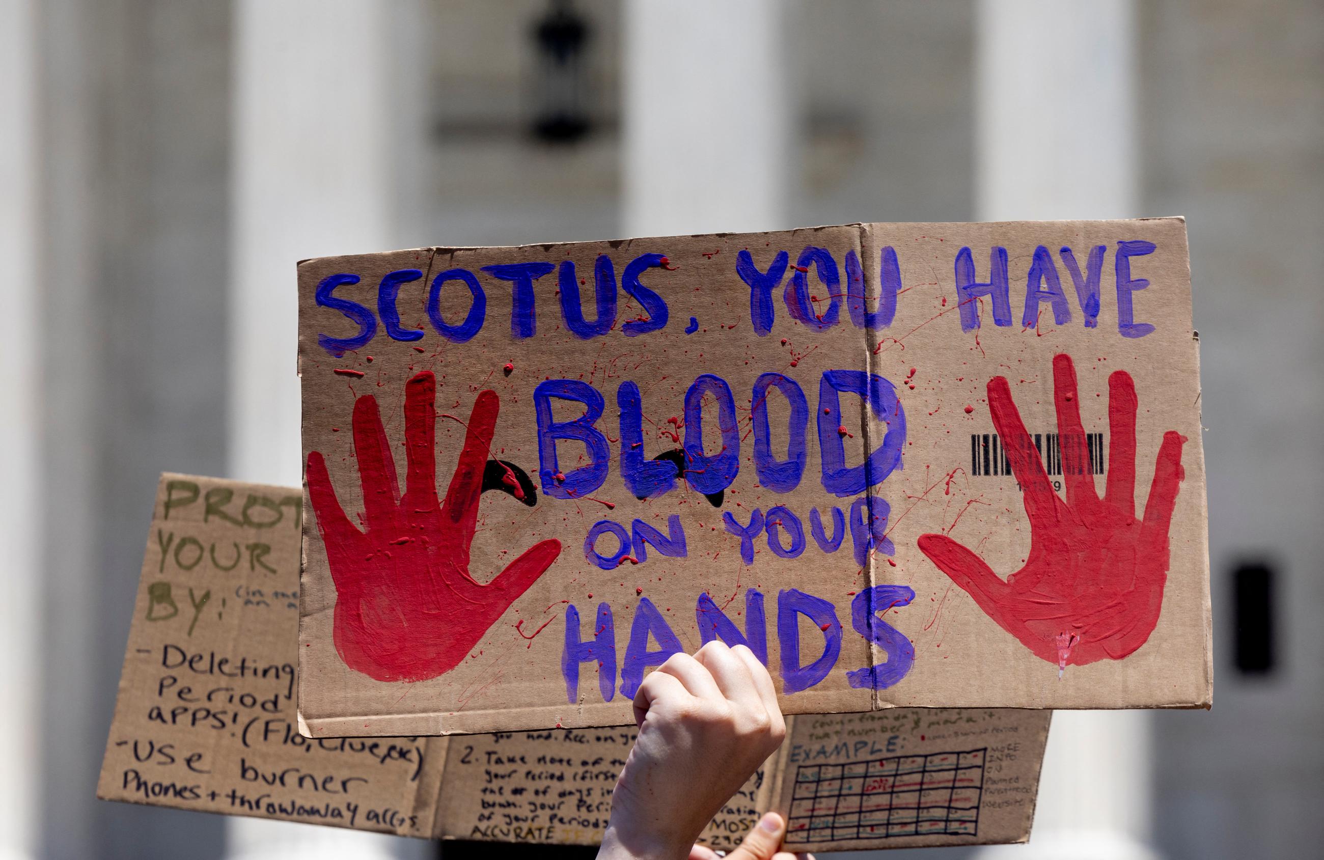 a cardboard signs reads "SCOTUS you have blood on your hands"