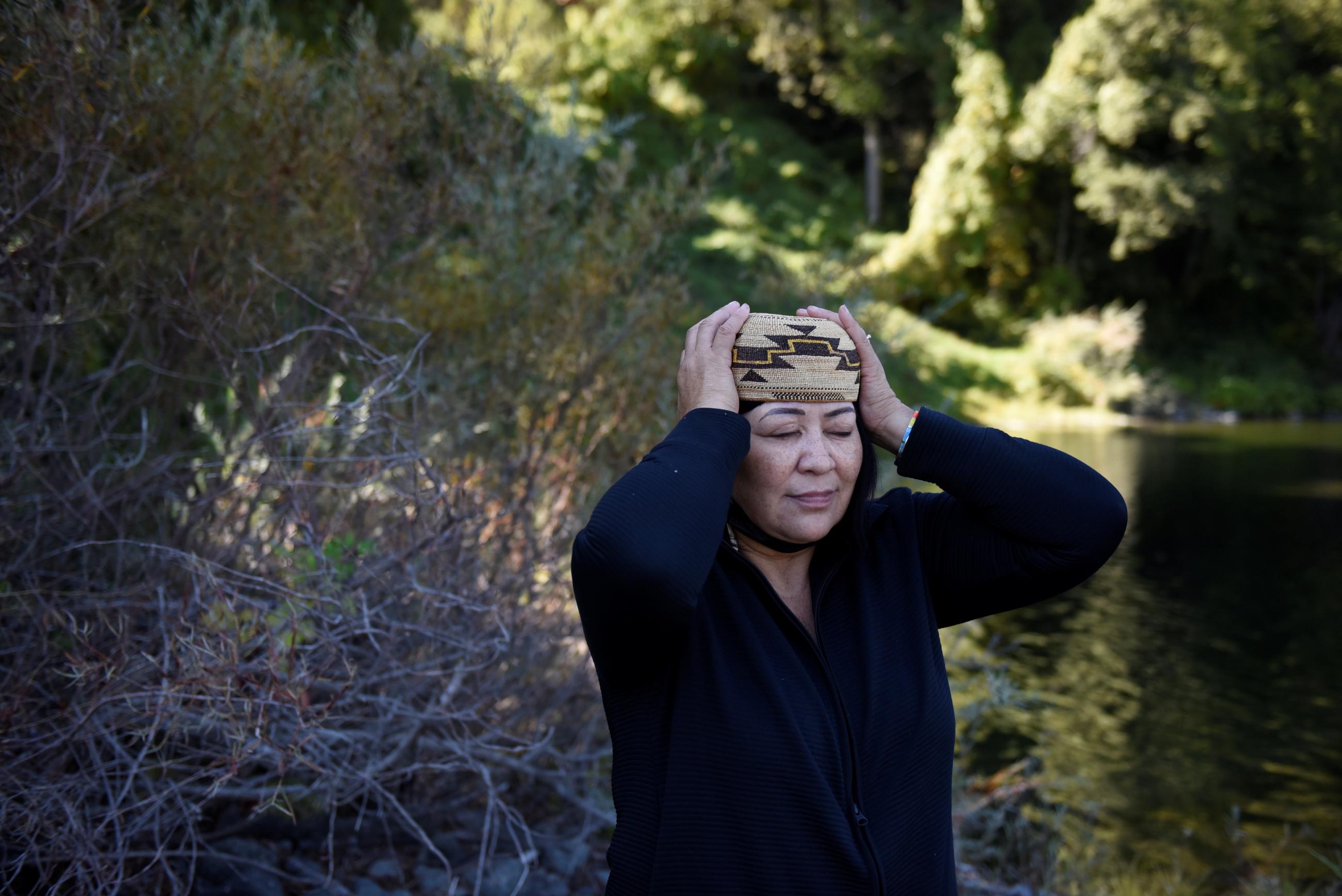 an indigenous American woman wearing a dark blue tunic places a traditional cap on her head
