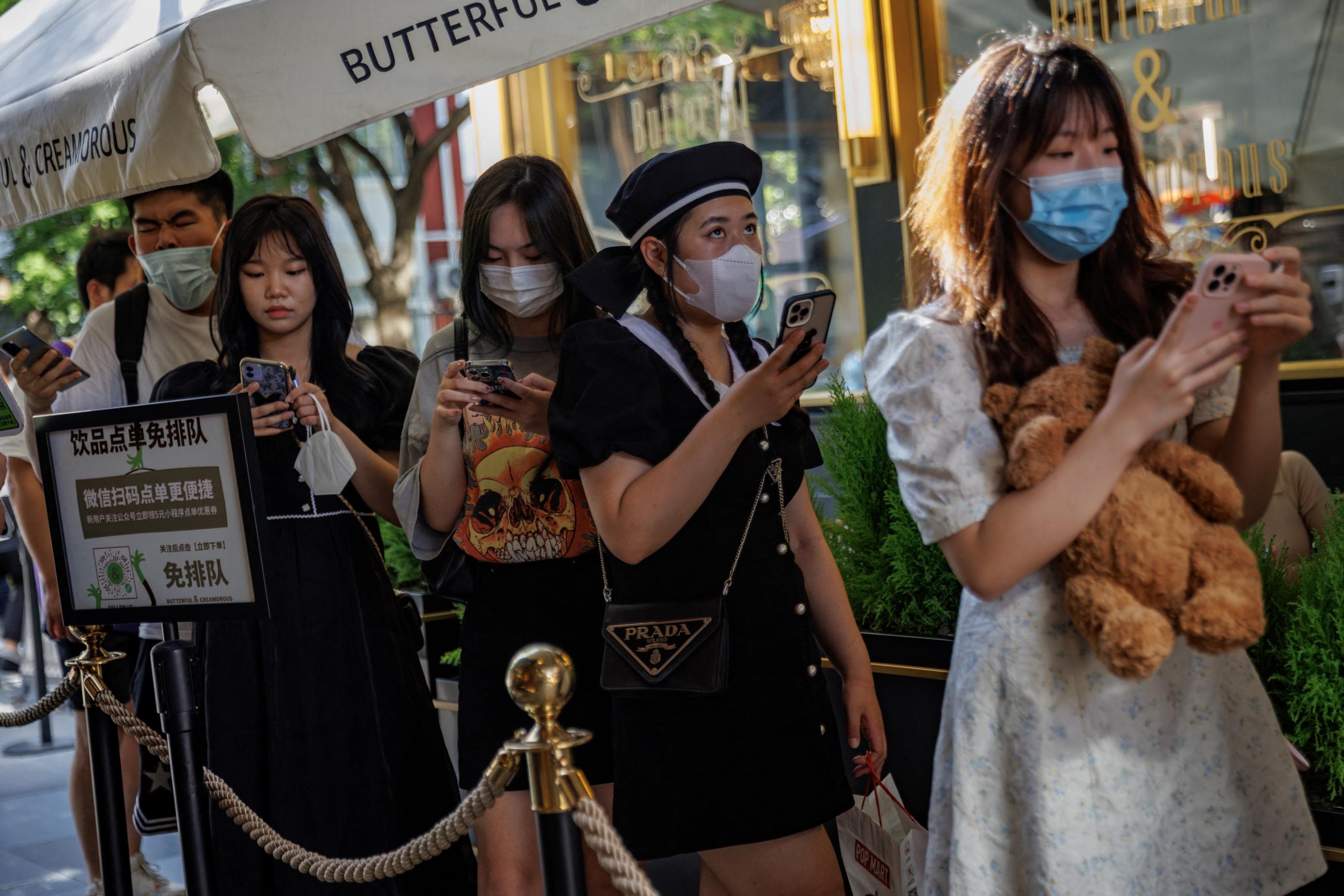 Young women wearing COVID masks line up holding teddy bears outside of a trendy cafe in a shopping area in Beijing, China, on July 14, 2022. 