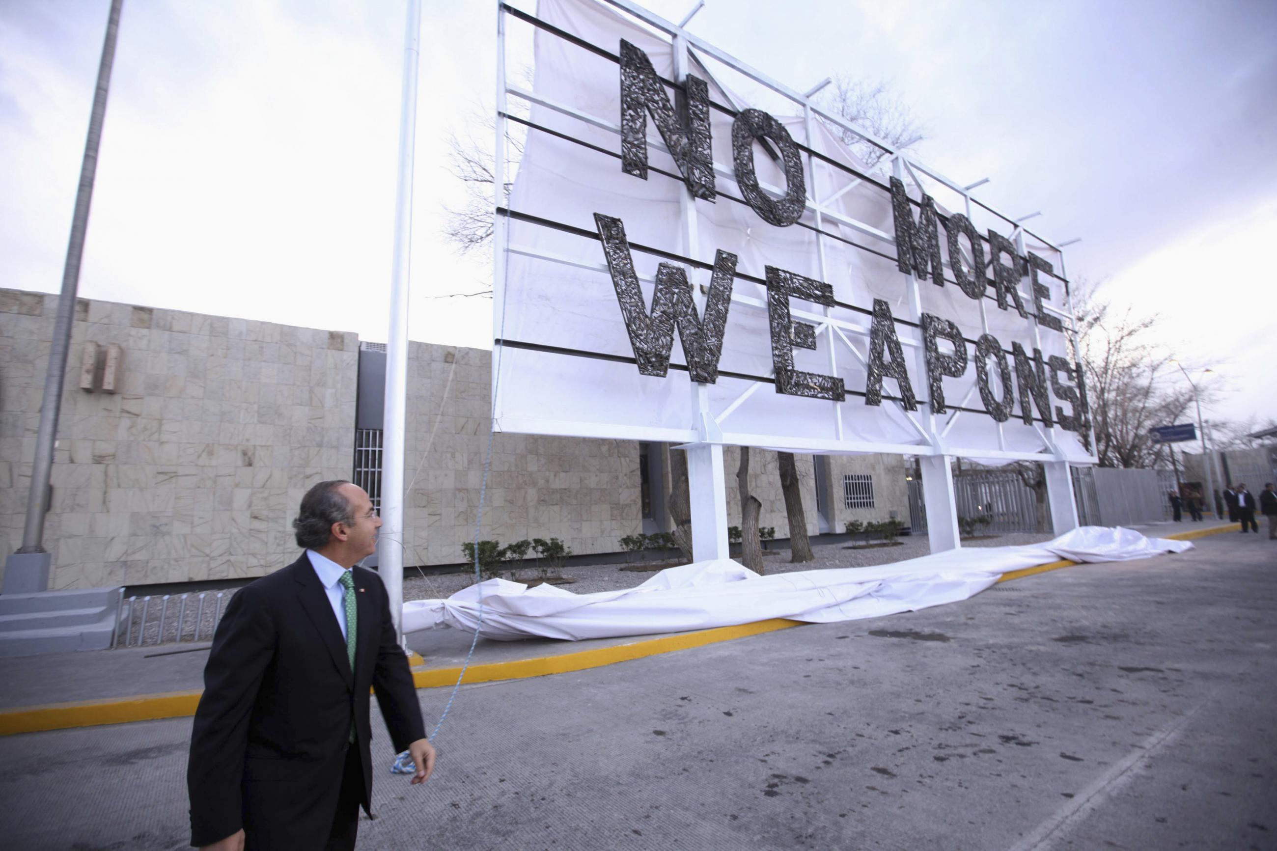 Mexican President Felipe Calderon wears a black suit as he glances behind after unveiling a white banner with big black letters reading "No More Weapons" during an event next to the Cordova-Americas international border crossing bridge in the border city of Ciudad Juarez on February 16, 2012.
