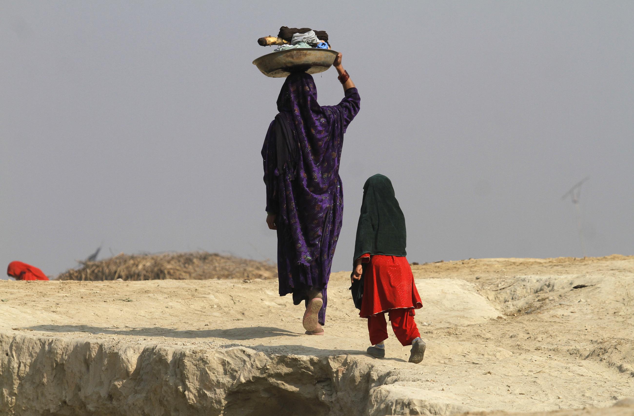 A woman walking alongside her child carries laundry on her head