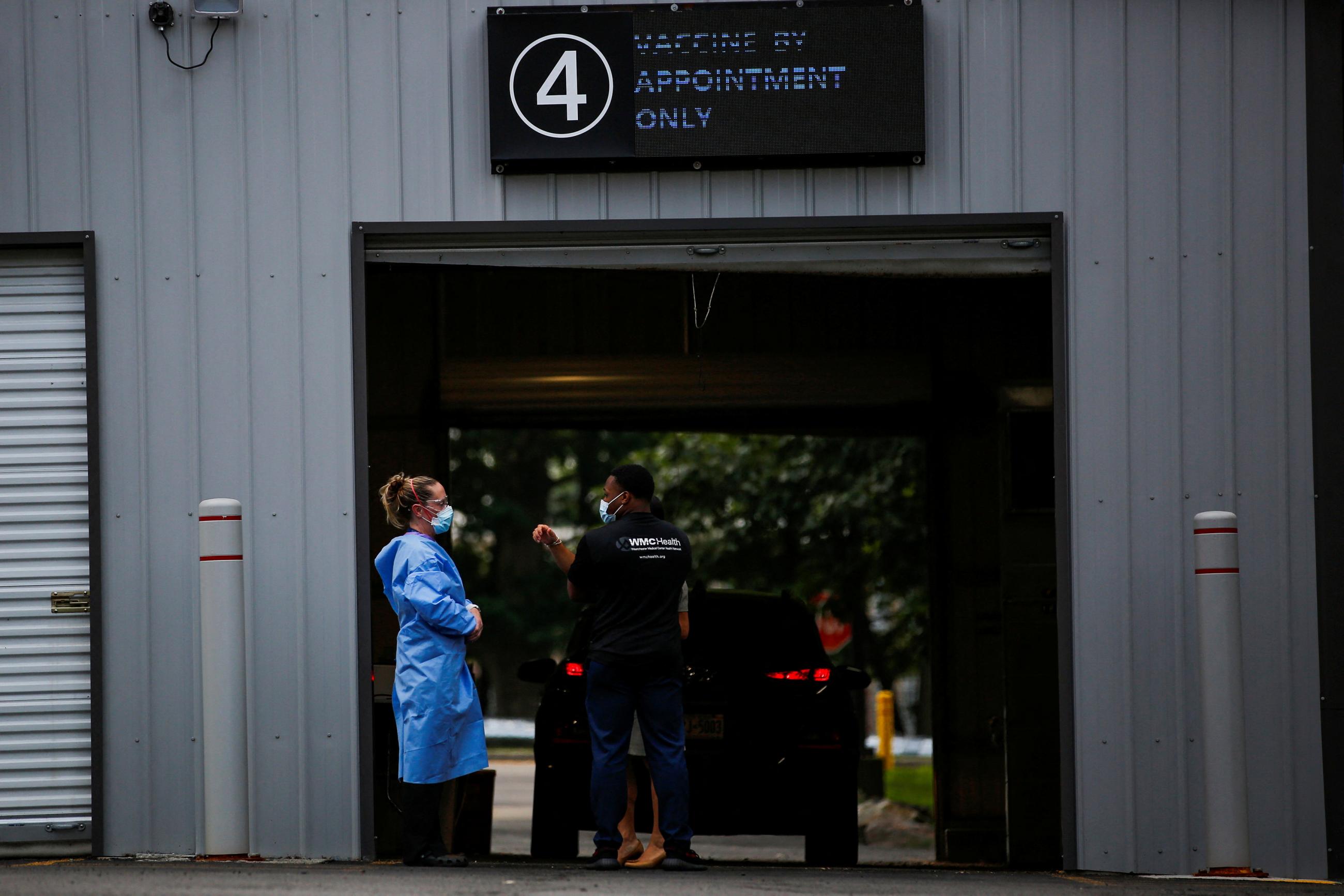 Male and female staff members of the Westchester Medical Center are pictured wearing PPE in front of a car port