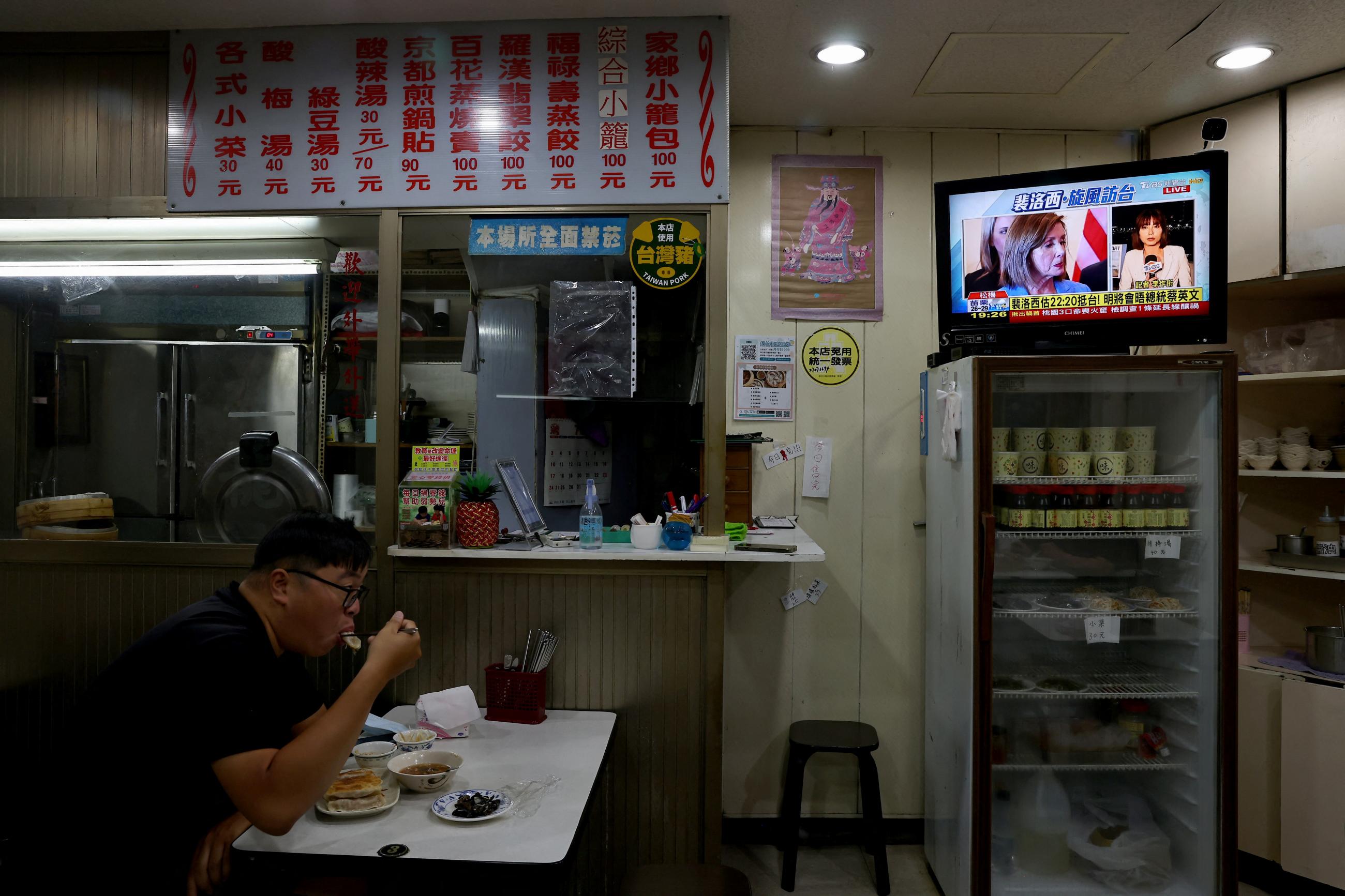 A man is photographed eating  by himself at a dinner in Taipei, Taiwan, as a TV in the background displays footage of Nancy Pelosi's visit to the island
