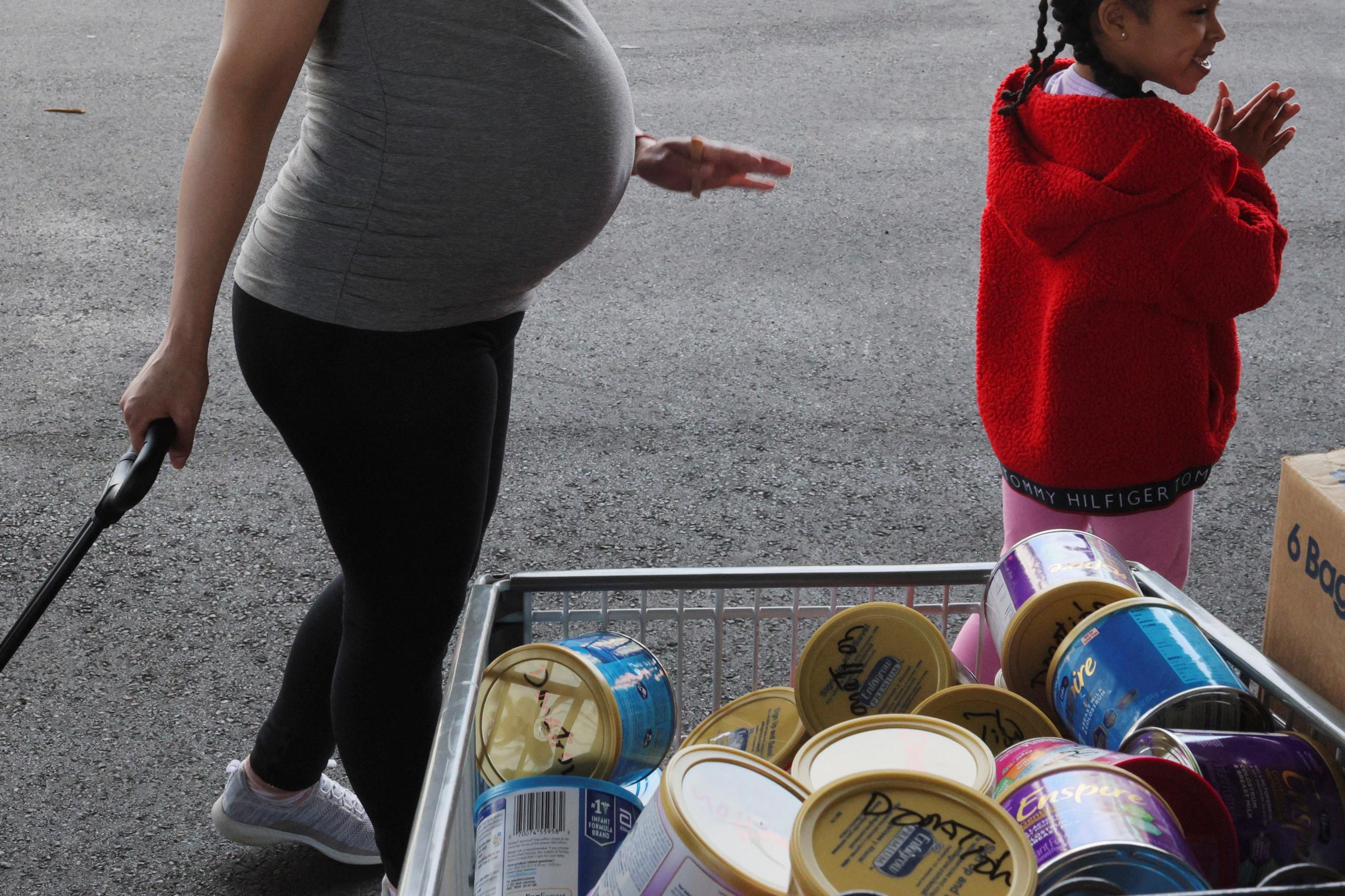 the silhouettes of a pregnant woman and her young daughter are seen against a gray pavement backdrop