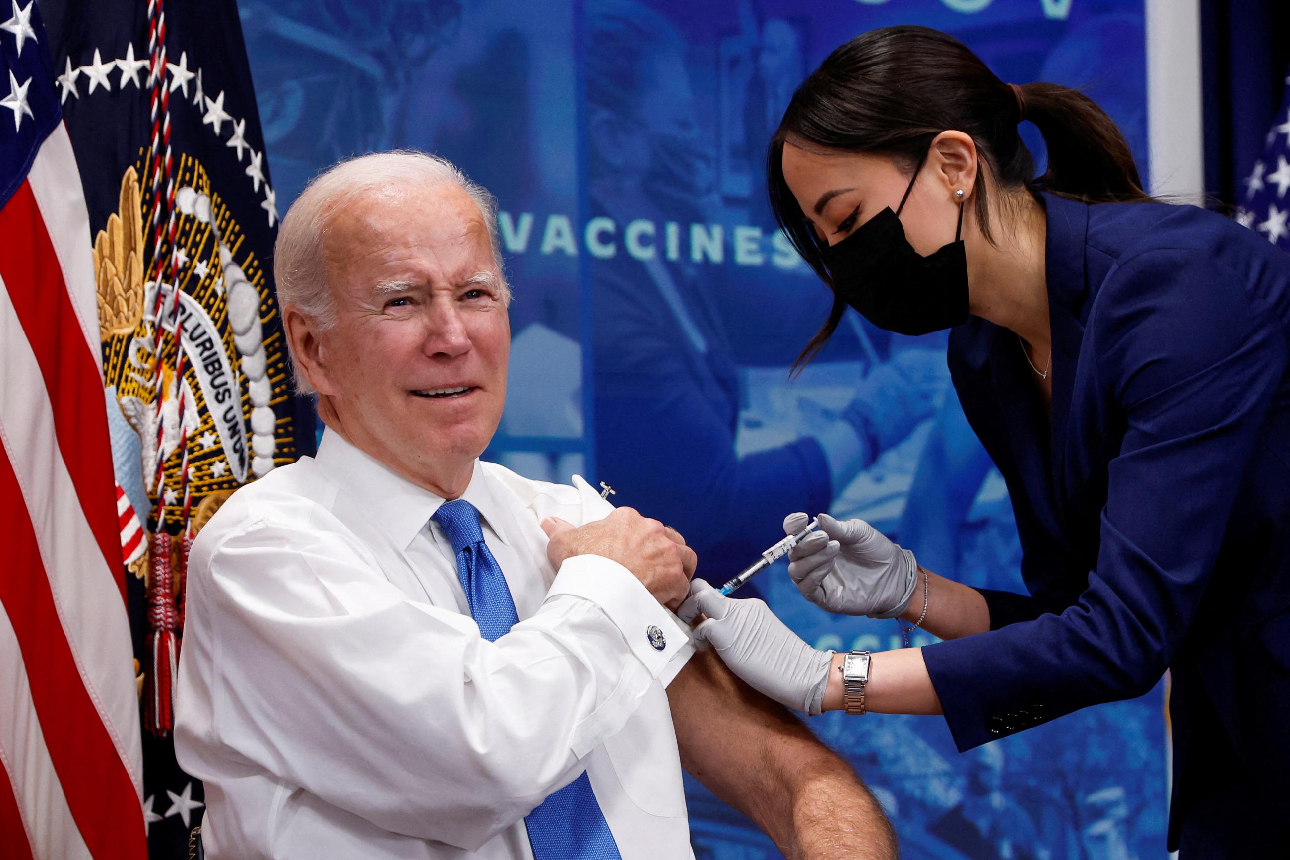 U.S. President Joe Biden, sleeve rolled up on his white shirt, receives a COVID-19 vaccine from a health worker wearing a dark blue suit at the launch of a new plan for Americans to receive booster shots and vaccinations, at the White House, Washington, DC, on October 25, 2022. 