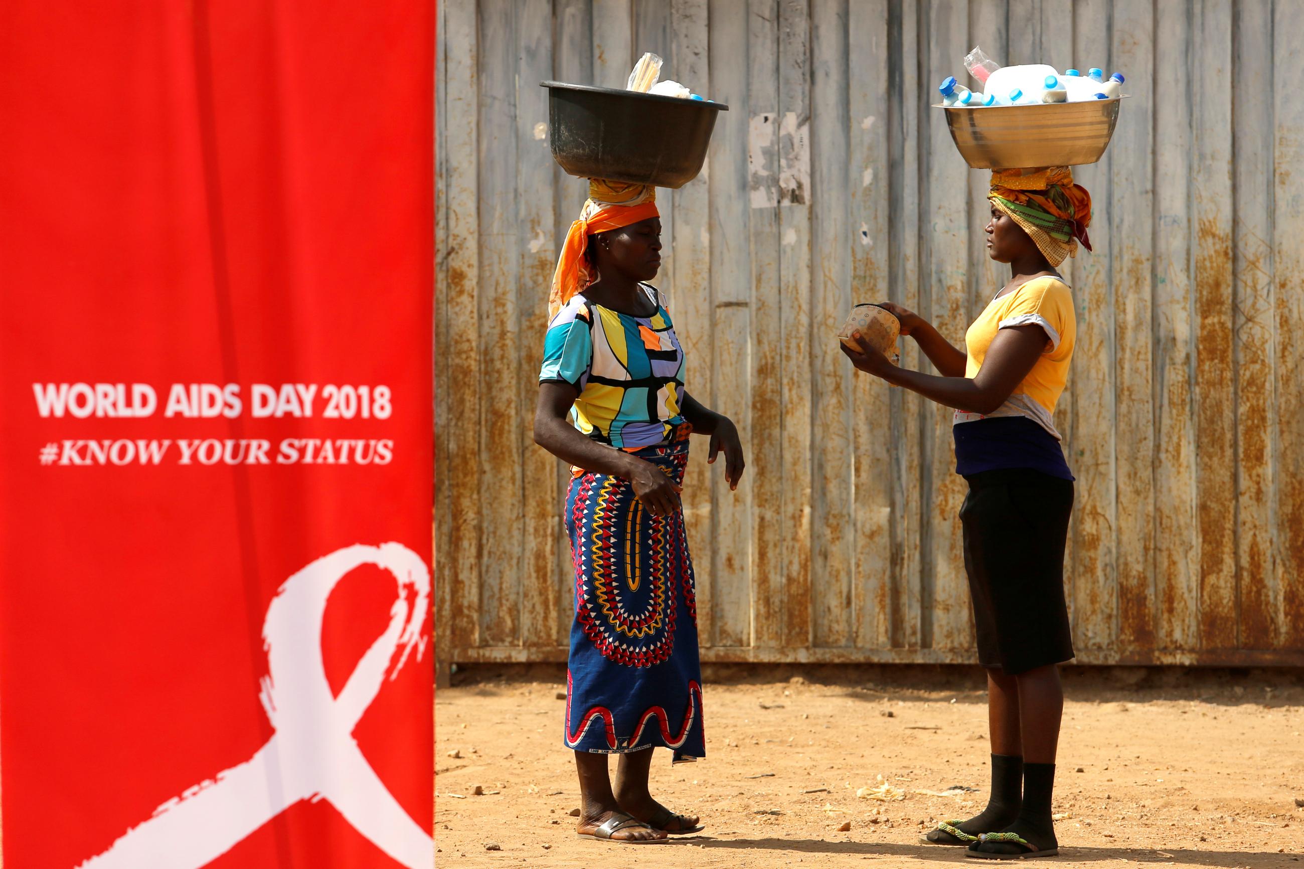 Two women stand near a bright red banner during an HIV/AIDS awareness campaign on World AIDS Day at the Kuchingoro IDP camp for internationally displaced persons, in Abuja, Nigeria, on December 1, 2018.