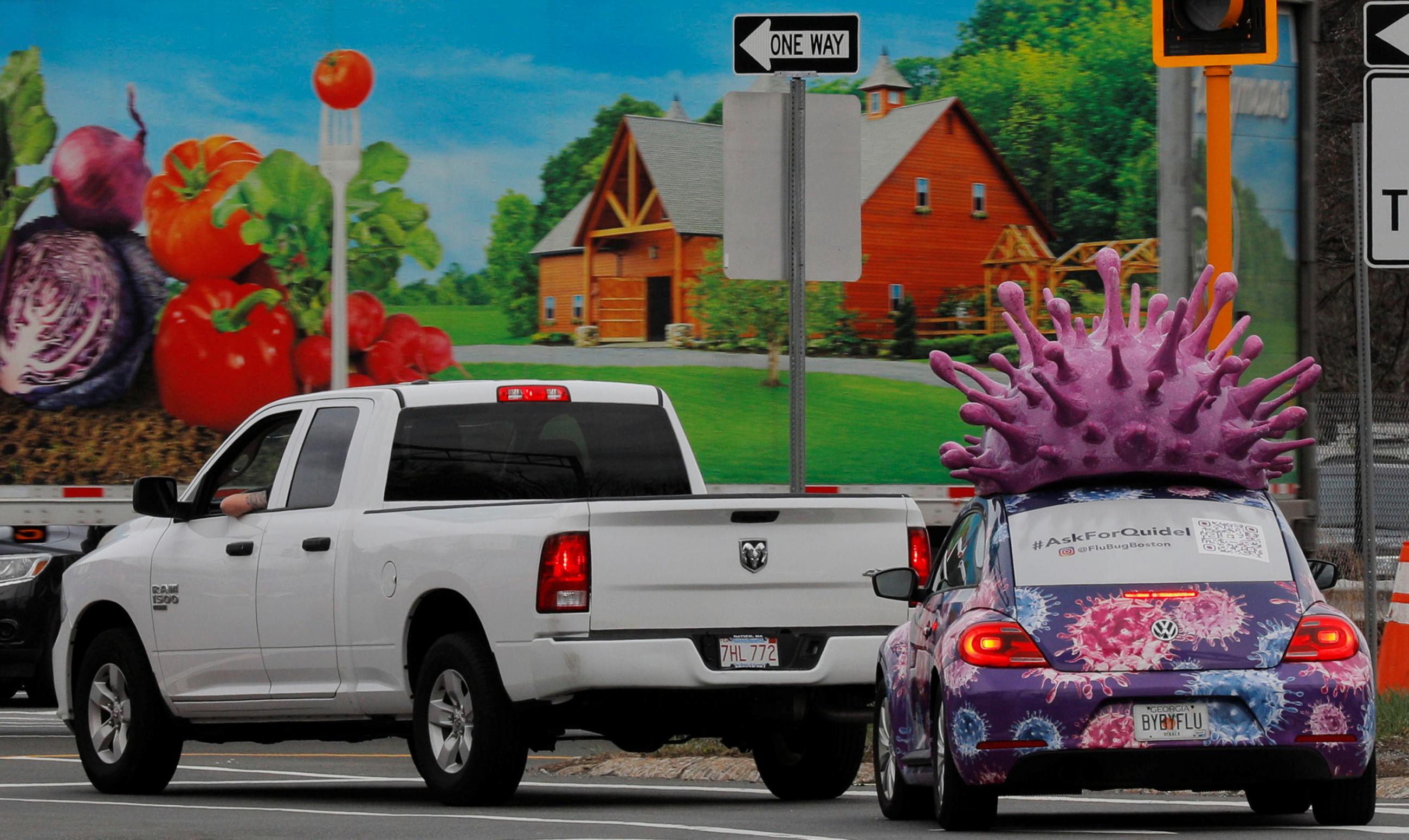 A colorful car advertising test kits for the flu and the coronavirus disease waits at a traffic light. It has a large purple  model of an influenza virus on its roof, in Medford, Massachusetts, on March 31, 2021. REUTERS/Brian Snyder
