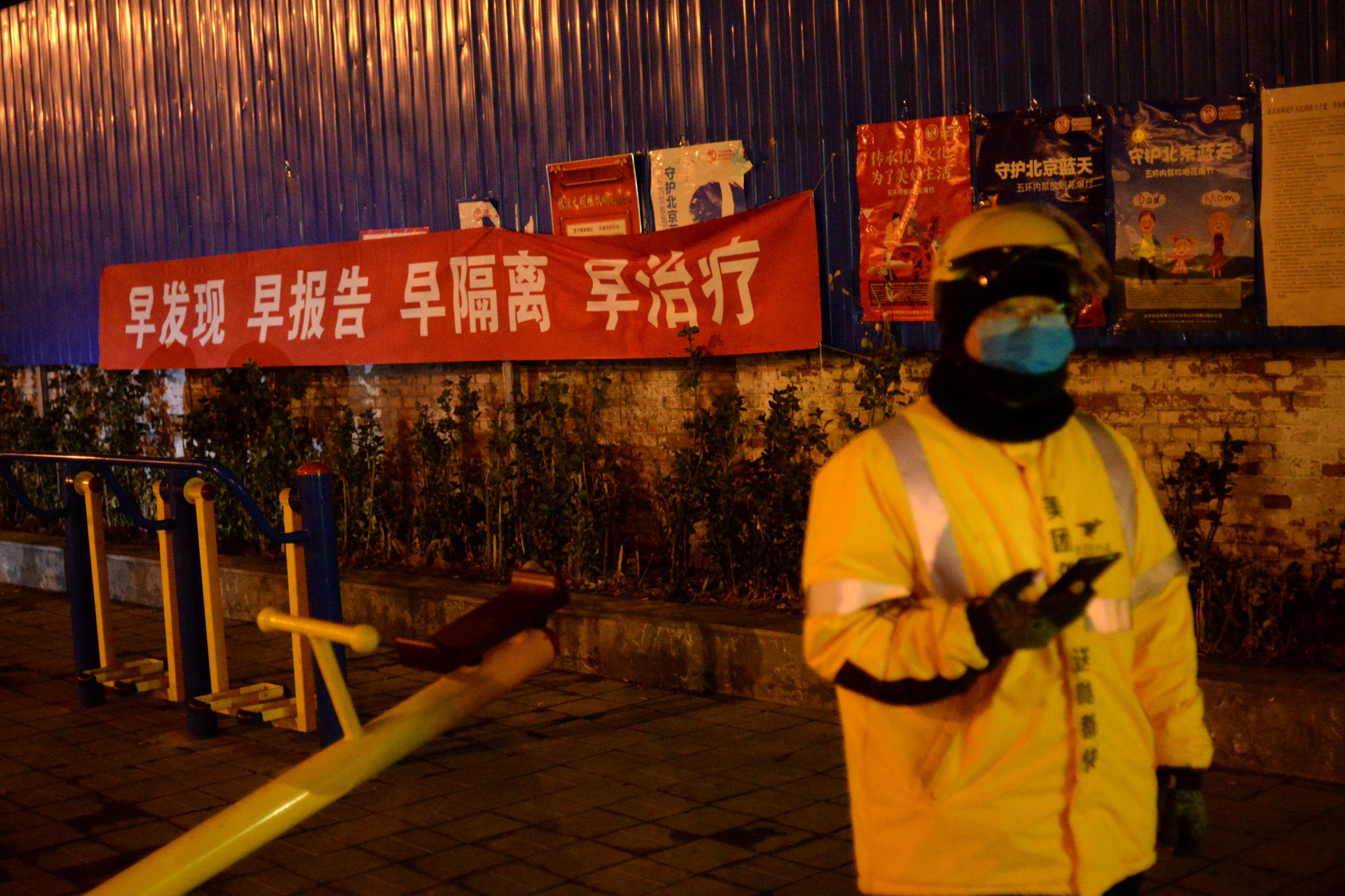 A deliveryman waits next to a propaganda banner, following an outbreak of COVID-19, Beijing, China February 11, 2020. The banner reads, "Detect early, report early, isolate early, treat early".