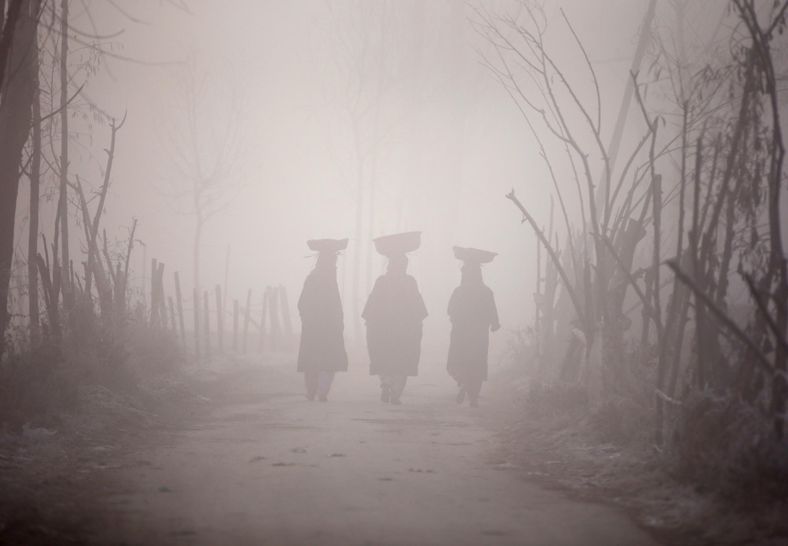 Kashmiri women carry baskets on their heads as they walk along the road amid dense fog on a cold morning in Srinagar, India, on November 30, 2015.