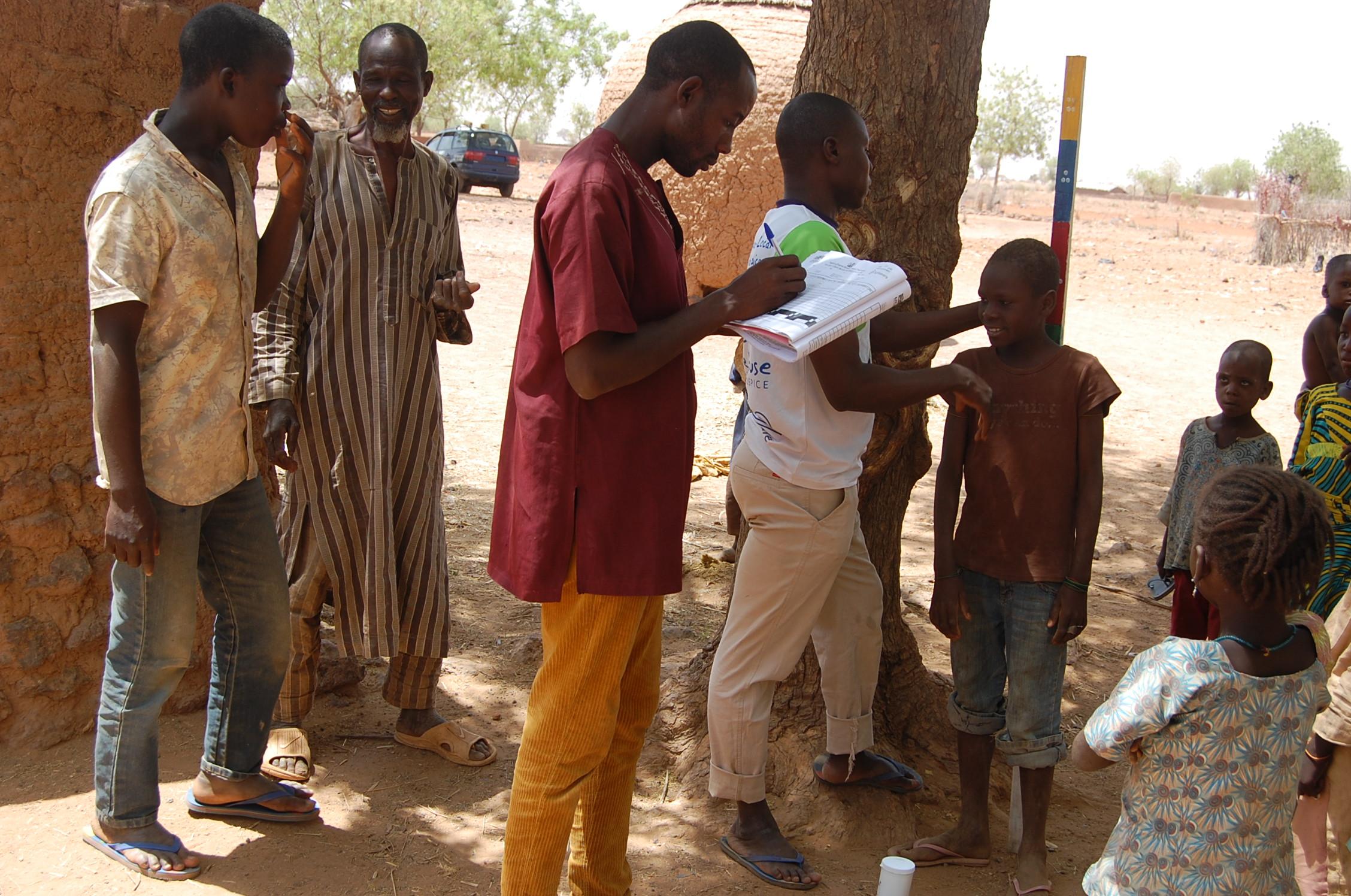 Kassimu, a health worker who has been selected as a community leader for the NTD programme, measures a young boy with a dose pole to determine the amount of medication they need to treat and prevent river blindness in Nigeria. 