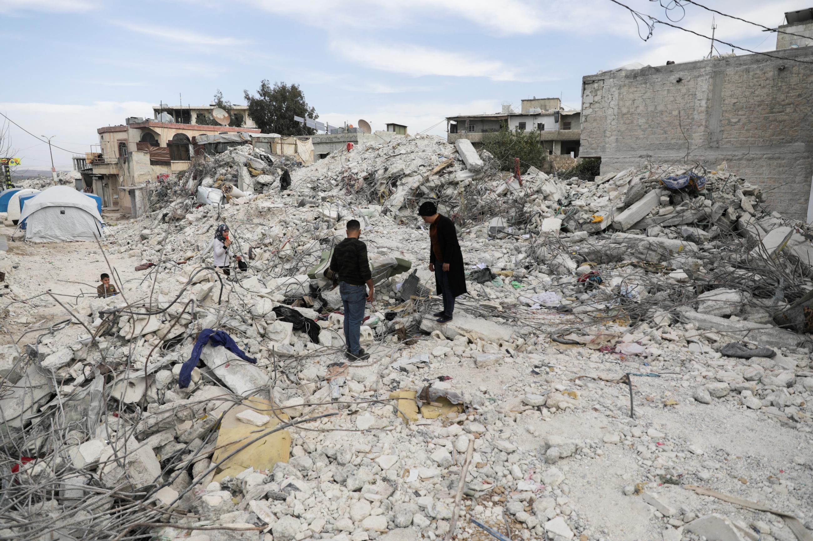 Two men stand on rubble from a building that collapsed in last month's deadly earthquake in the rebel-held town of Jandaris, Syria, on March 12, 2023. 
