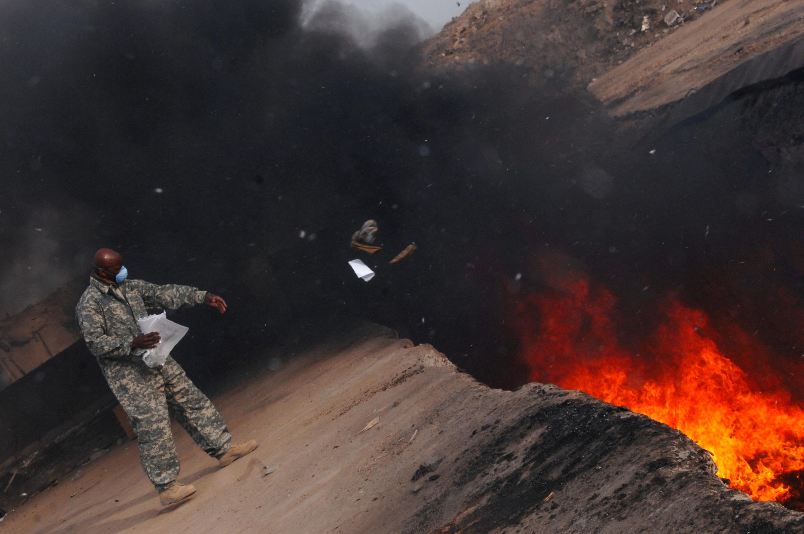 Master Sgt. Darryl Sterling, 332nd Expeditionary Logistics Readiness Squadron equipment manager, tosses unserviceable uniform items into a burn pit at Balad Air Base in Iraq, March 10, 2008.