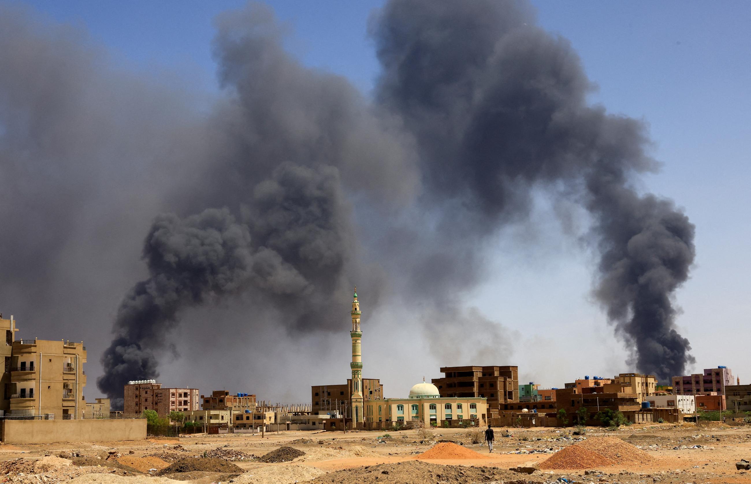 A man walks as smoke rises above buildings after aerial bombardment during clashes between the paramilitary Rapid Support Forces and the army in Khartoum North, Sudan, on May 1, 2023.