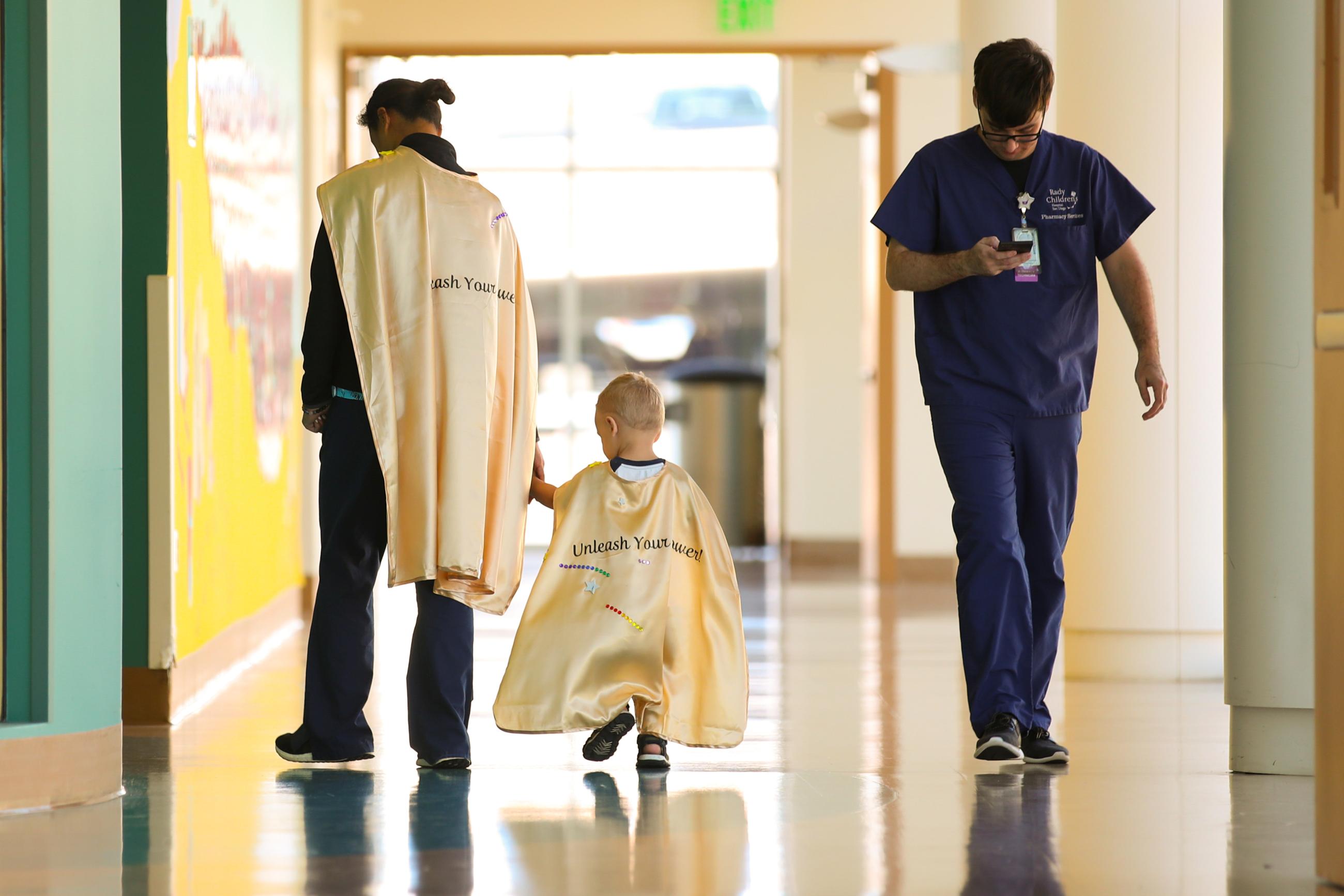 Two-year-old cancer patient Jimmy walks with his nurse back to his room at Rady's Children Hospital after participating in decorating golden capes that say "Unleash Your Power" to wear as superheroes as part of Childhood Cancer Month in San Diego, California, on September 4, 2019.