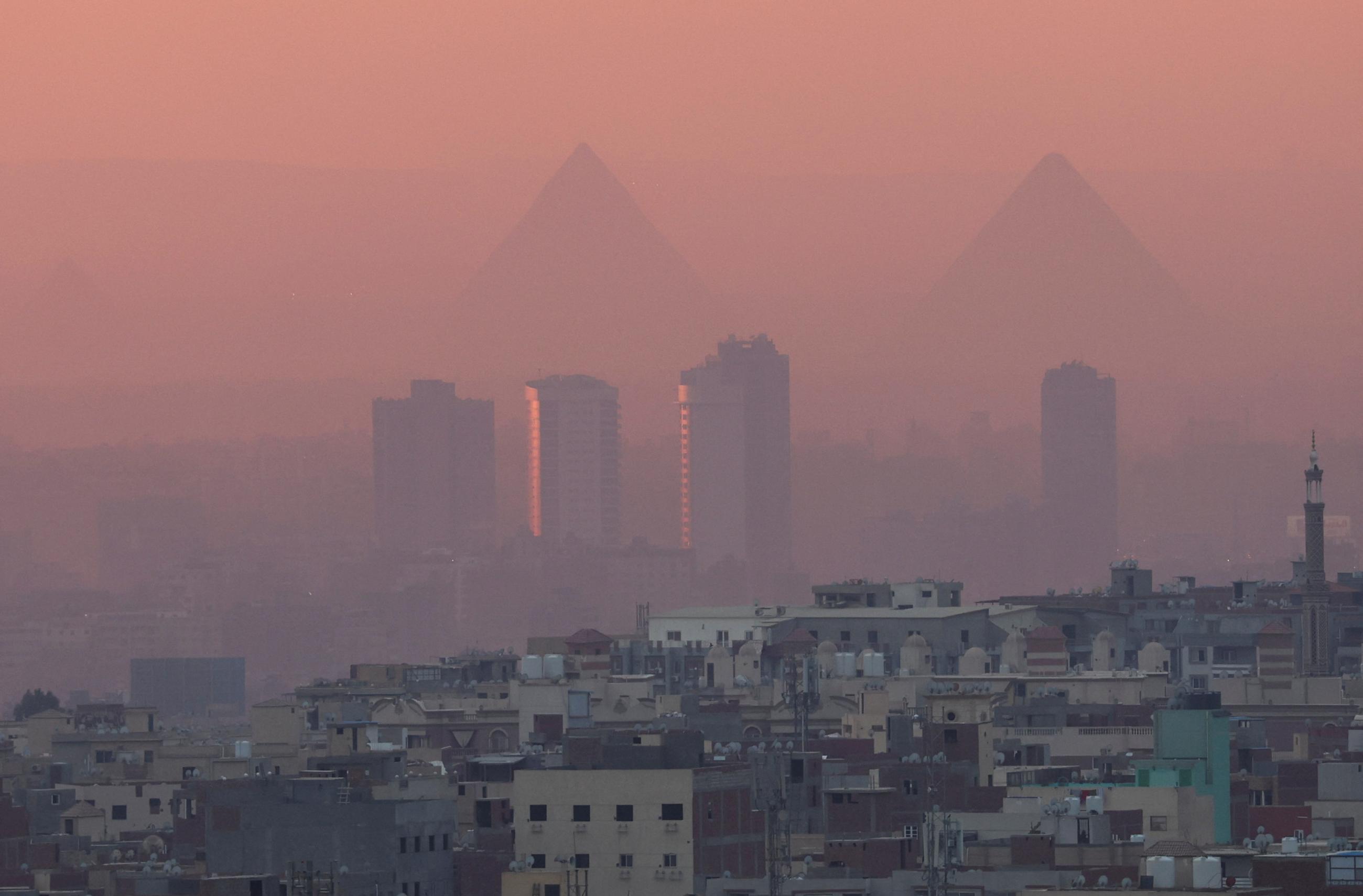 A view of old houses with hotels and the Great Pyramids during sunset with fog from air pollution over Egypt's capital of Cairo, February 5, 2023. 