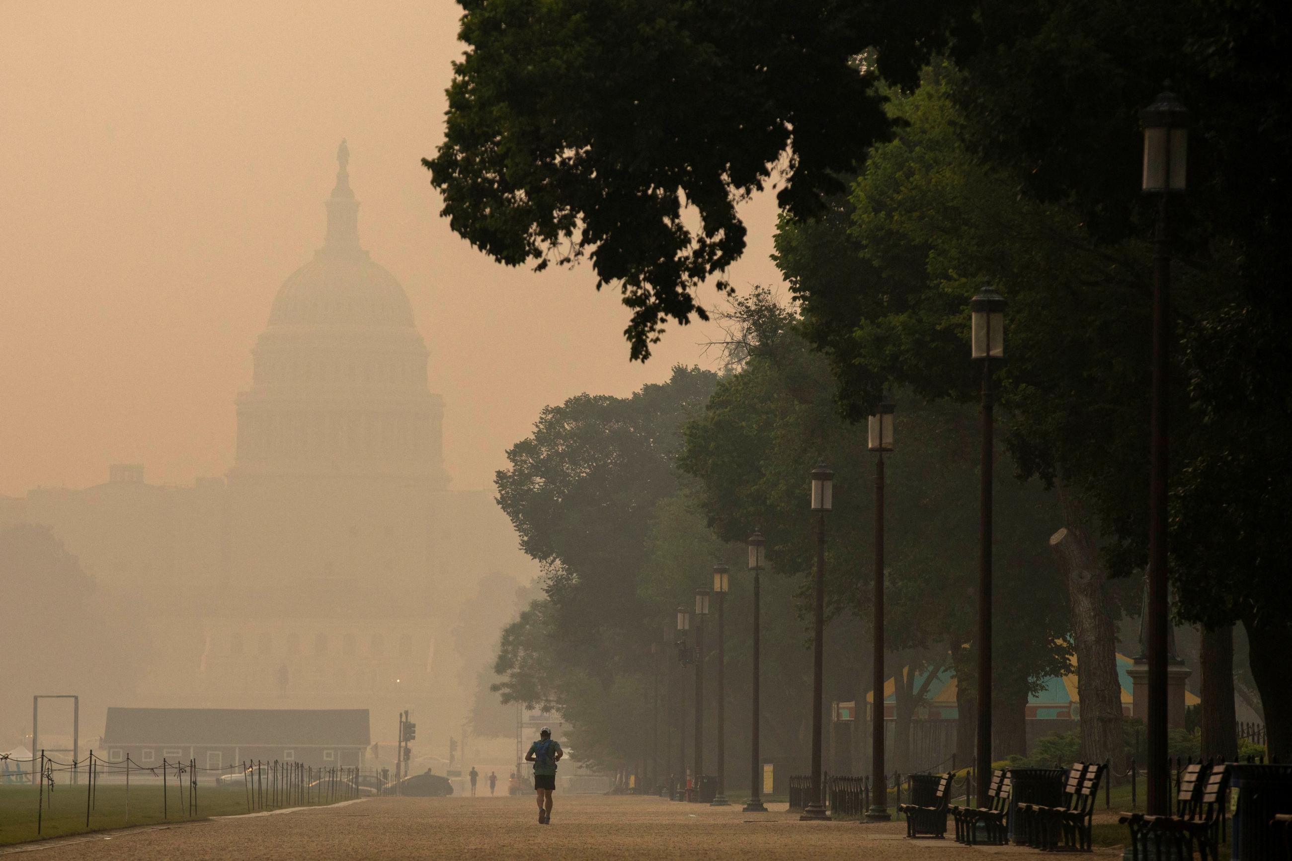 A person runs on the National Mall as the U.S. Capitol is seen shrouded in haze and smoke caused by wildfires in Canada, in Washington, DC, on June 8, 2023