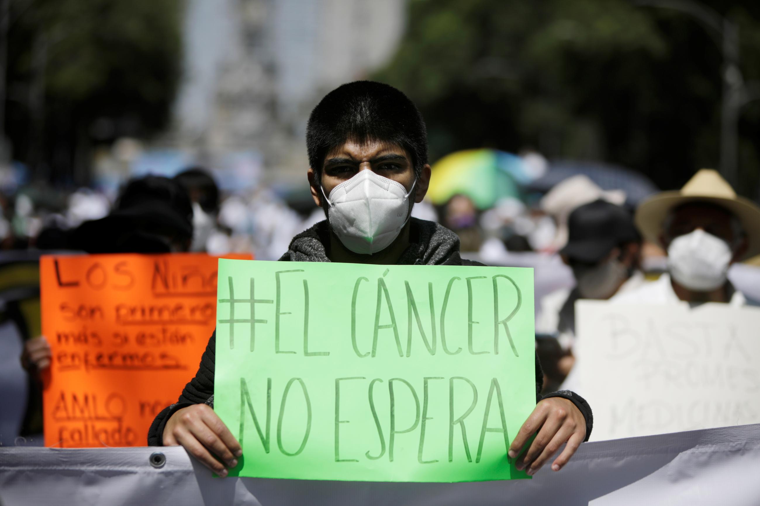 A youth with sunglasses and a face mask holds a sign that reads "cancer doesn't wait" in Spanish at a march in support of children and women with cancer in Mexico City, Mexico. 