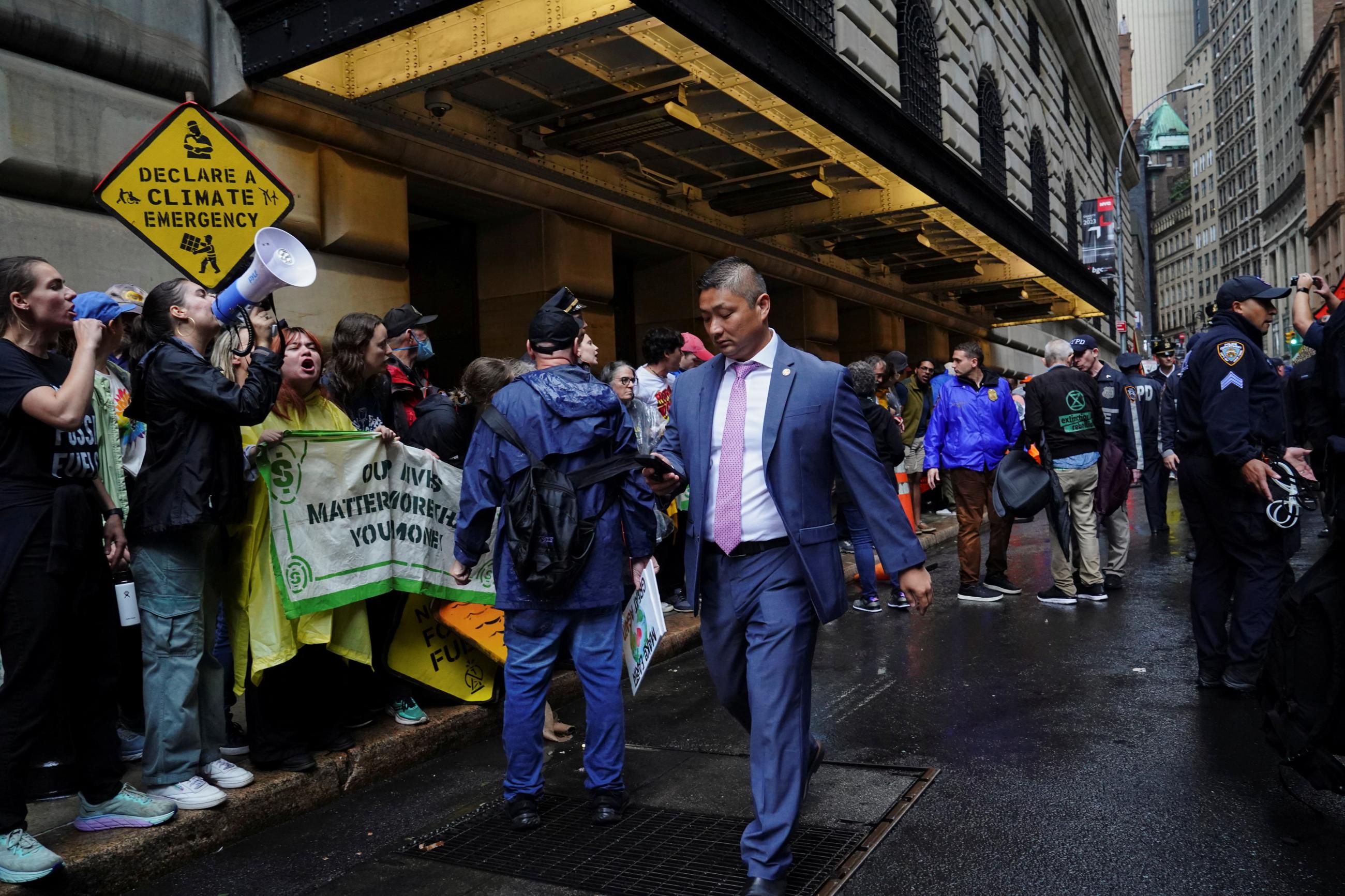 A man in a business suit walks past activists protesting outside the Federal Reserve Bank of New York during a demonstration calling for the U.S. government to take action on climate change and reject the use of fossil fuels during Climate Week in the Financial District of New York City, New York, U.S., September 18, 2023.